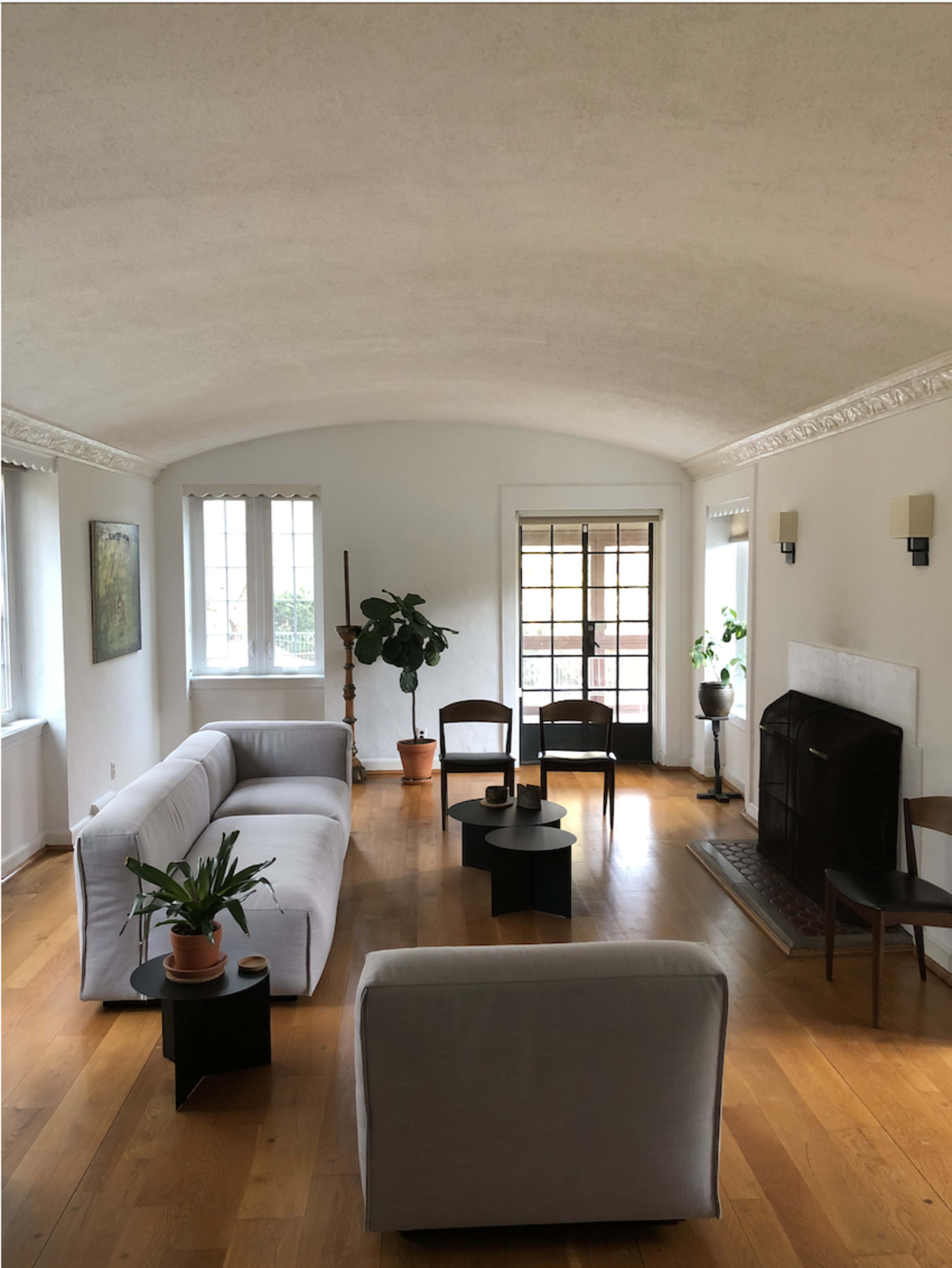 A spacious living room features a white sofa, two black chairs, a small table, and a fireplace, all arranged on polished wooden flooring.