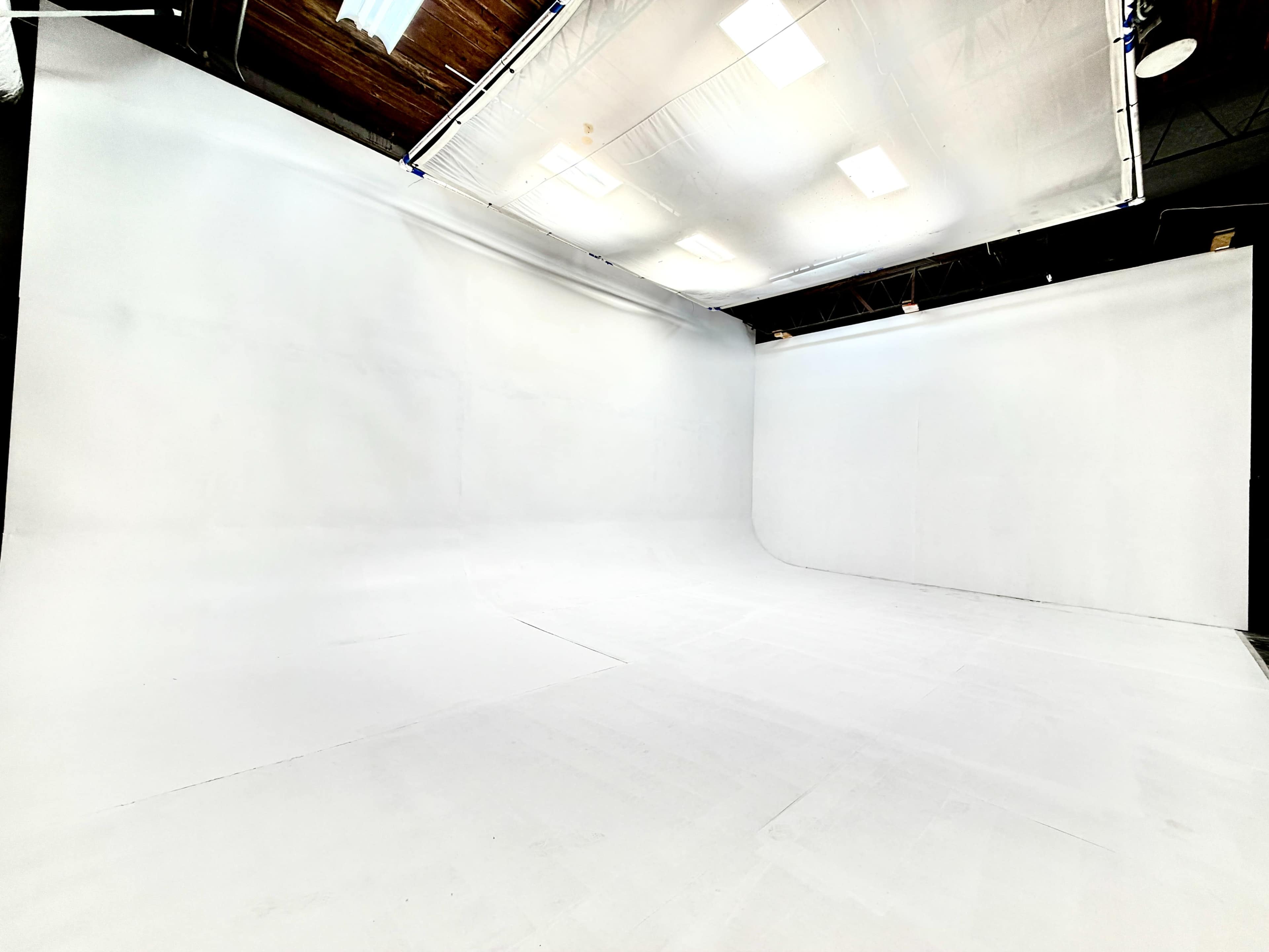 The image shows a spacious photography studio with white walls and a seamless white backdrop.