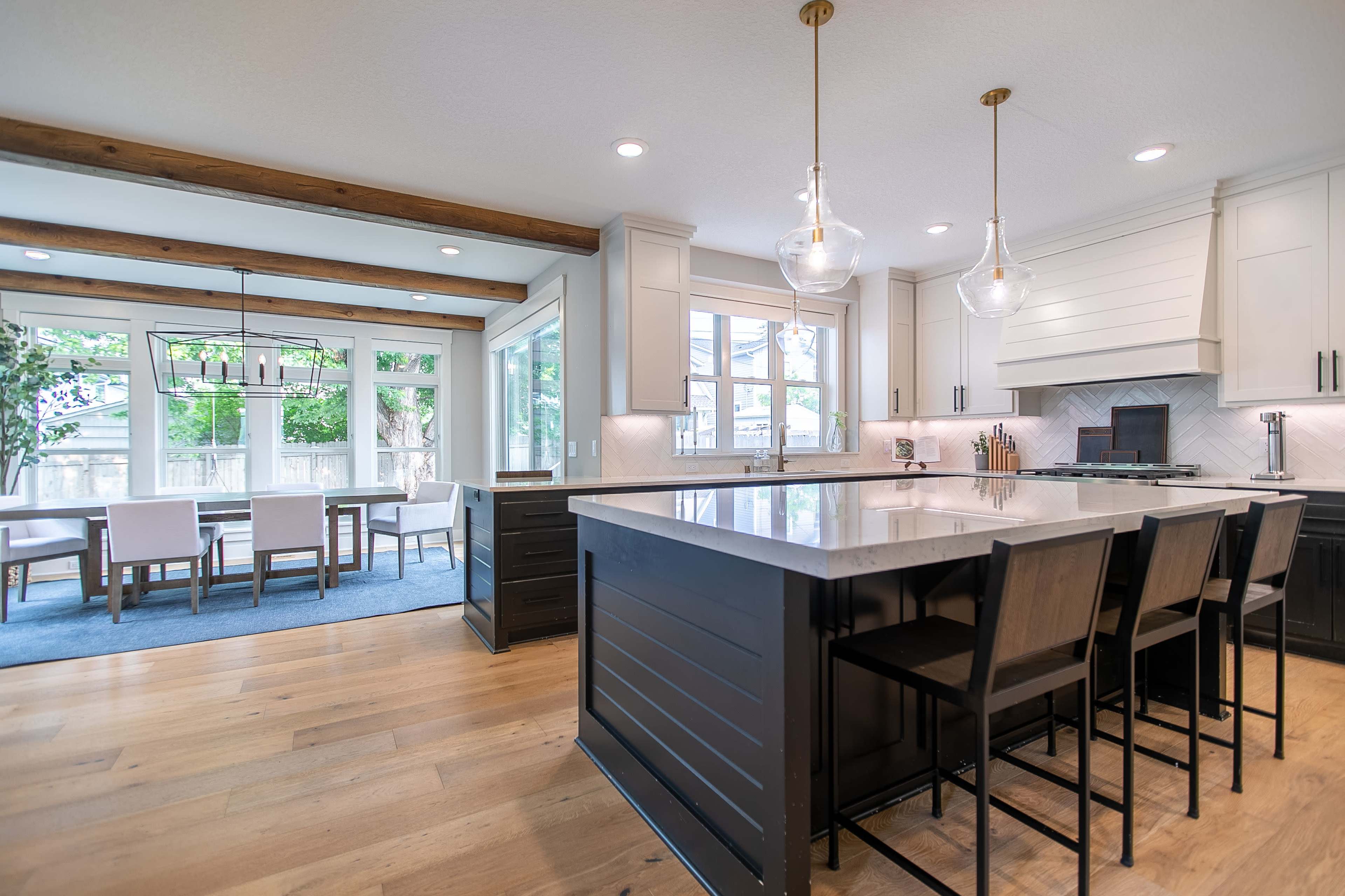 A modern kitchen features a large island with seating, white cabinetry, and a view of a dining area through large windows.