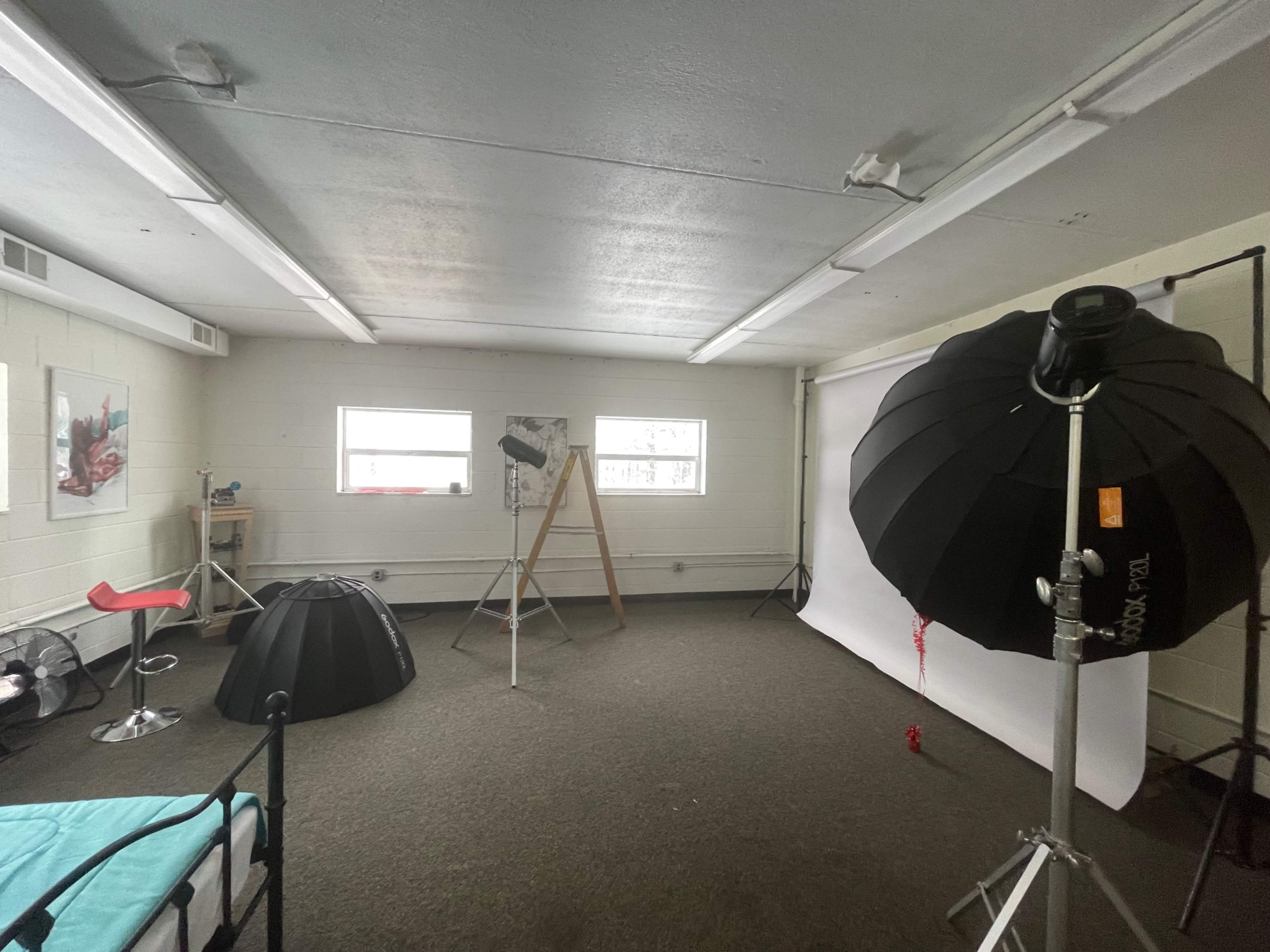 A photography studio with a backdrop, lighting equipment, a chair, and various props arranged in an empty, well-lit room.