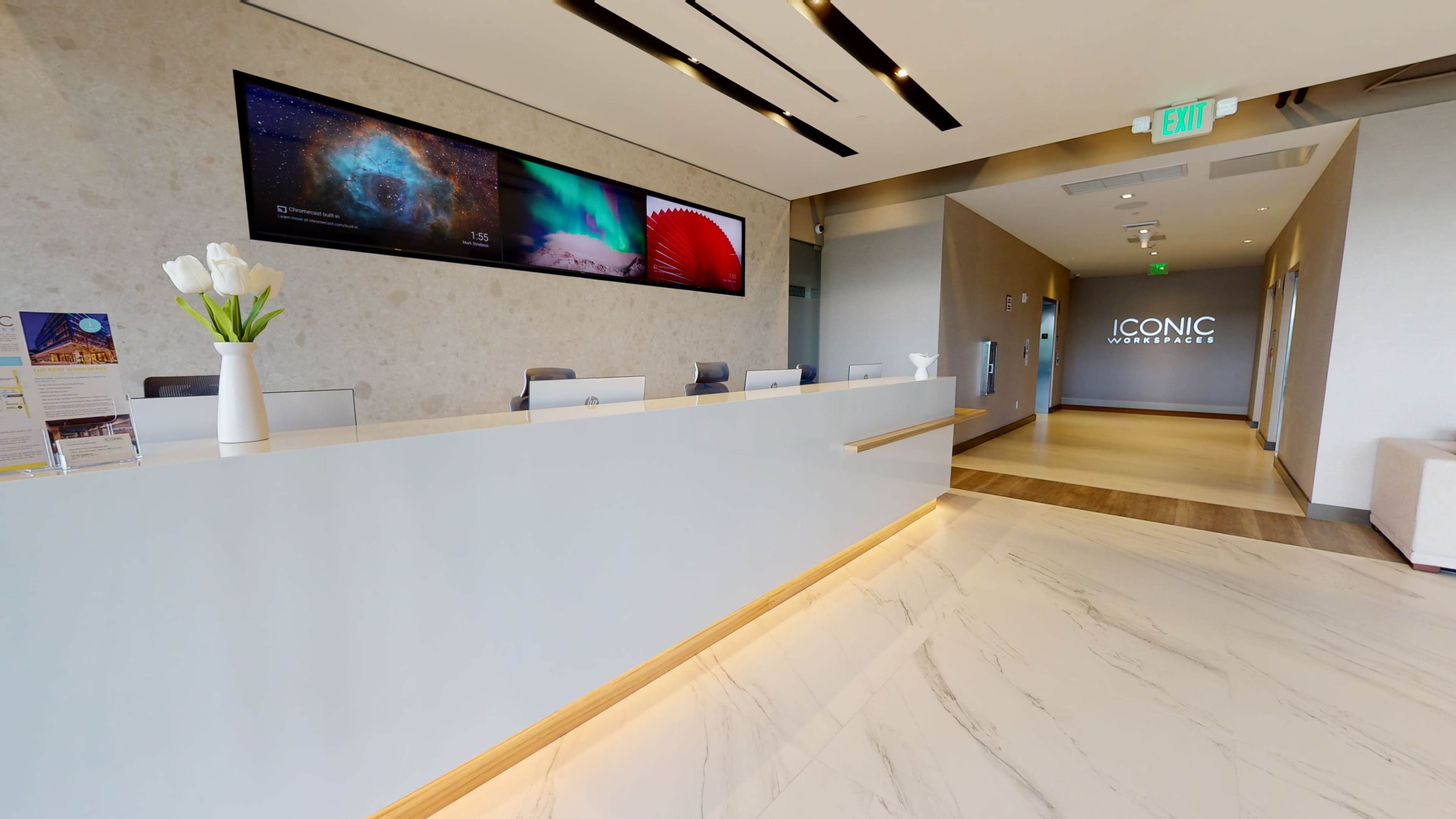 A modern reception area with a sleek white desk, digital displays on the wall, and polished marble flooring.