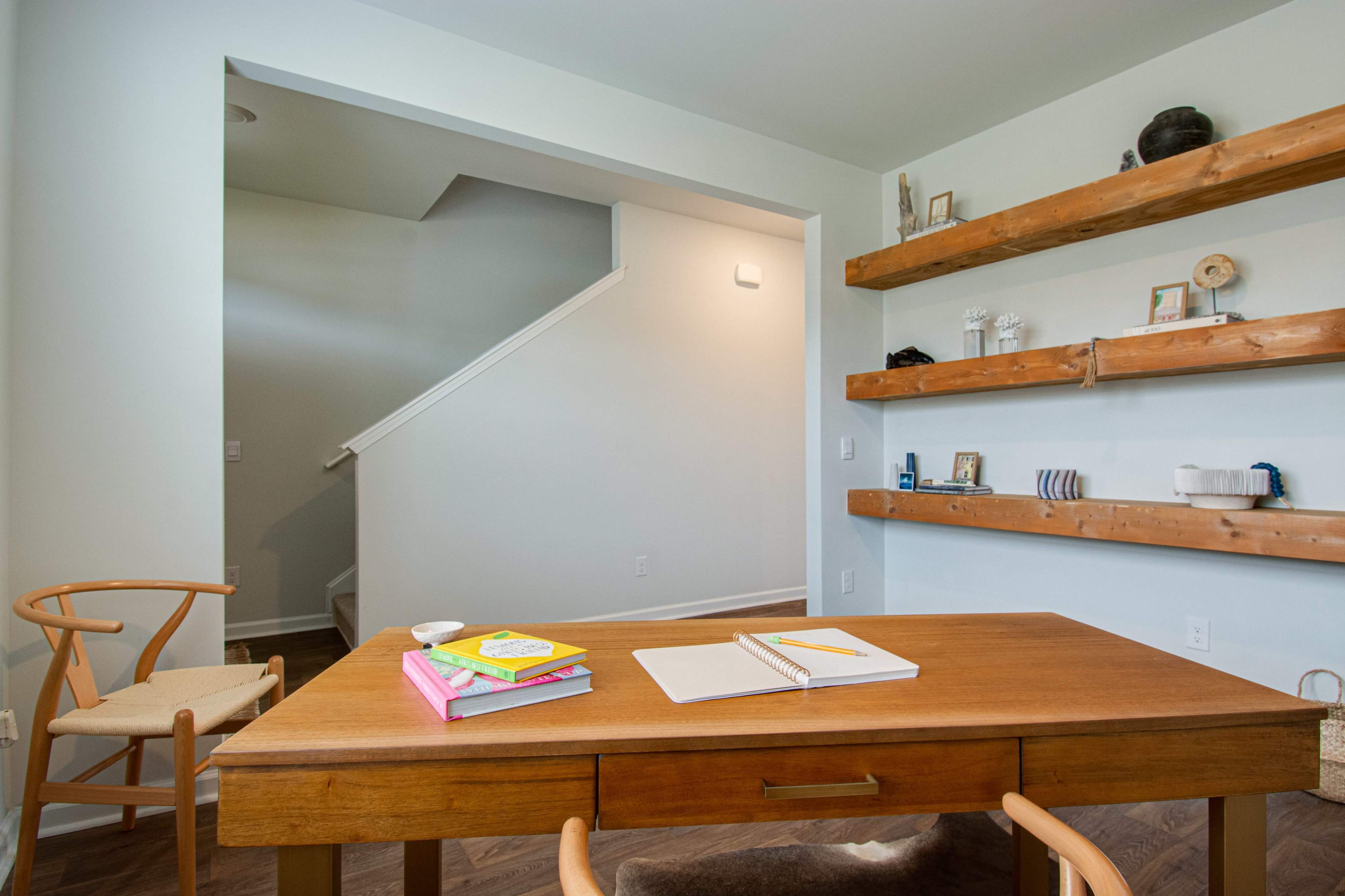 A home office with a wooden table, books on shelves, and a staircase in the background.