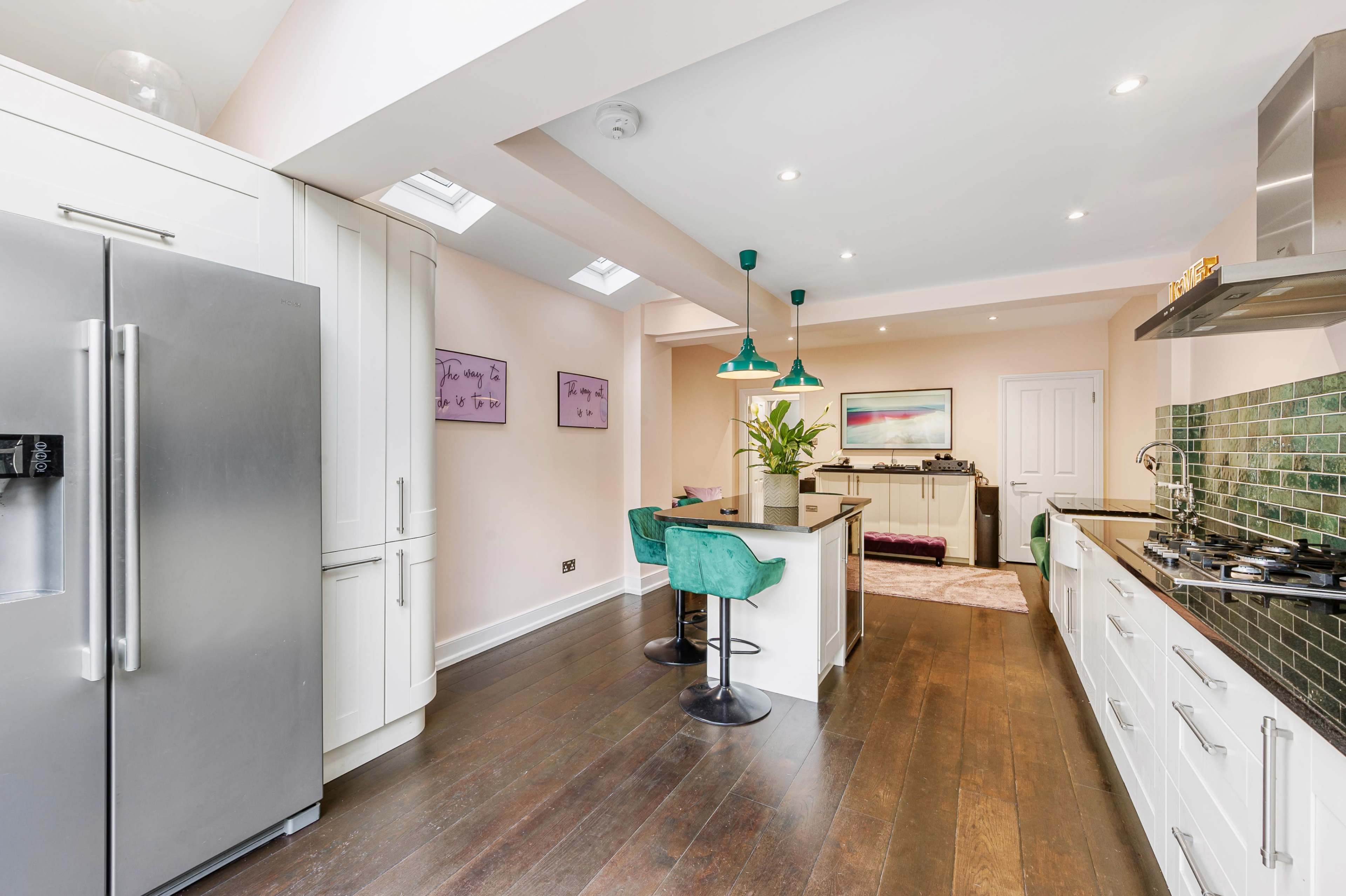 A modern kitchen features white cabinets, dark wooden flooring, and bar stools in front of an island with green accents.
