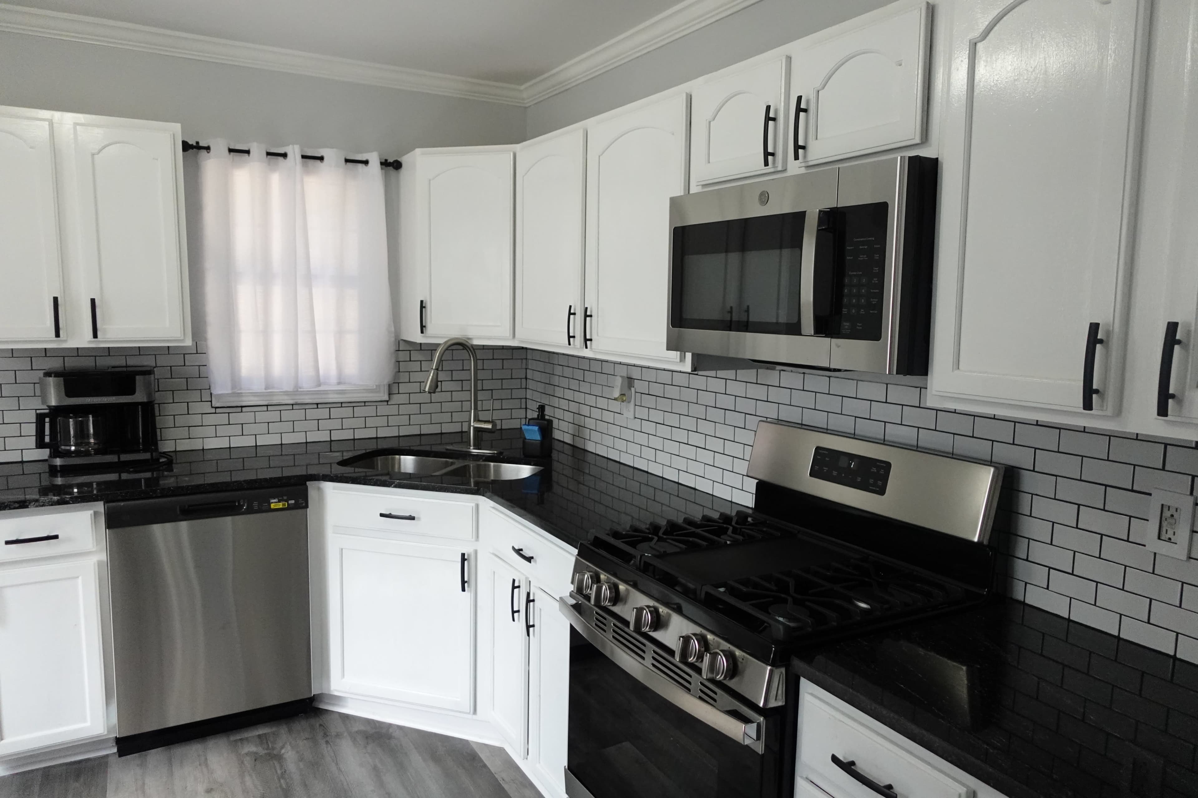 A modern kitchen with white cabinets, stainless steel appliances, a black granite countertop, and a tiled backsplash.