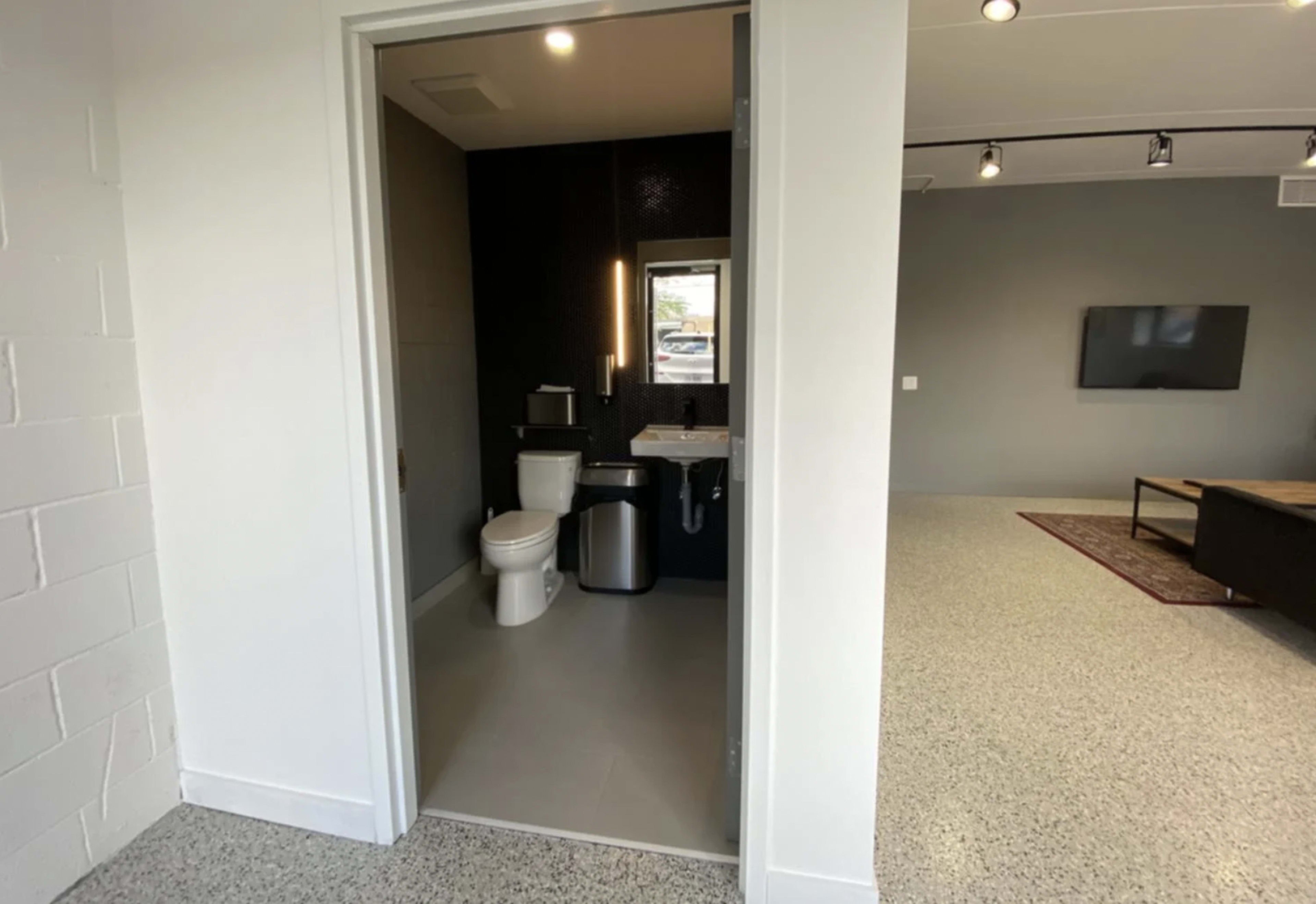A bathroom with a toilet and sink visible through an open door, adjacent to a modern living area with a television and a coffee table.