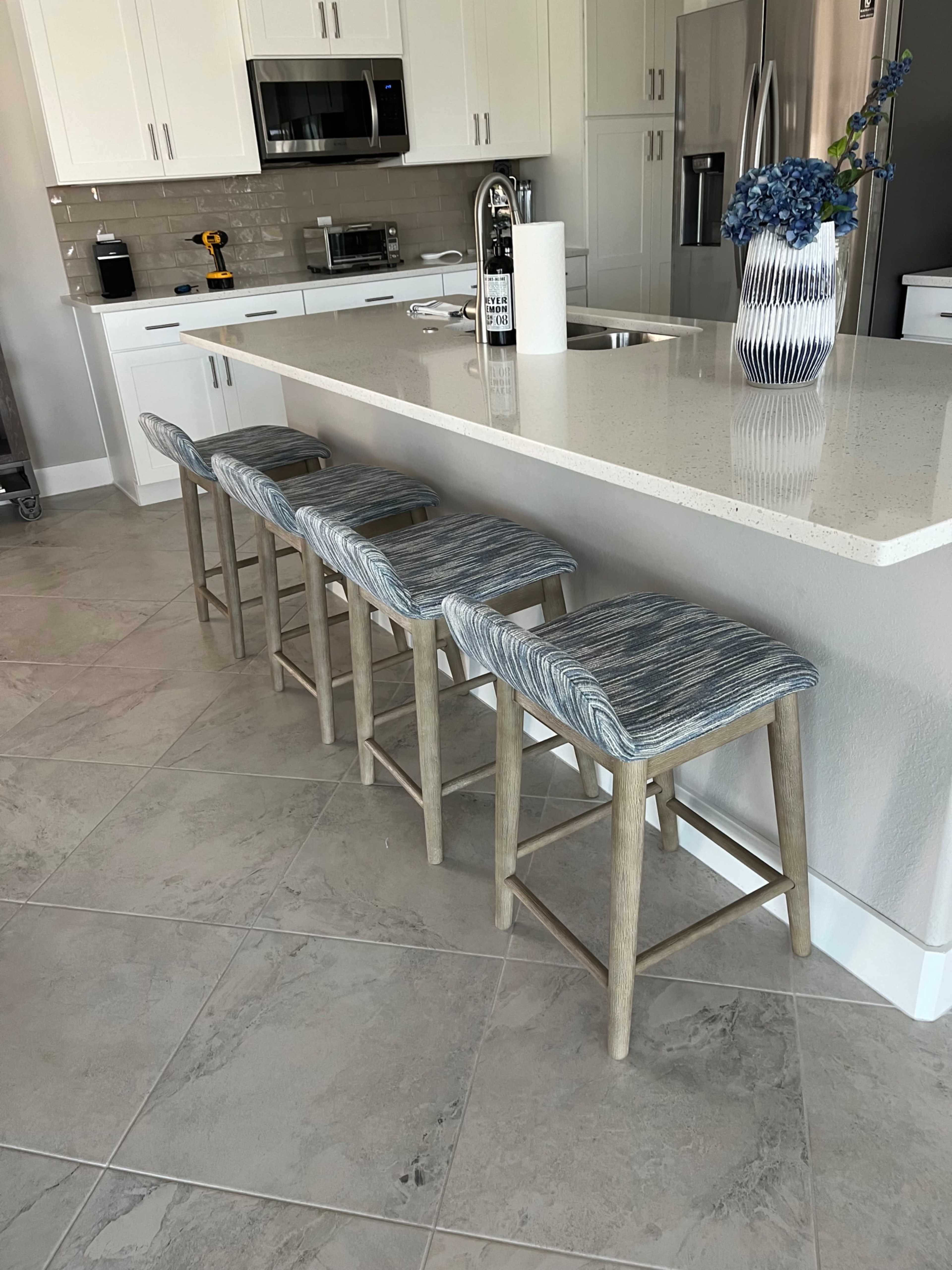 Four upholstered bar stools with wooden legs are lined up against a kitchen island in a modern kitchen.