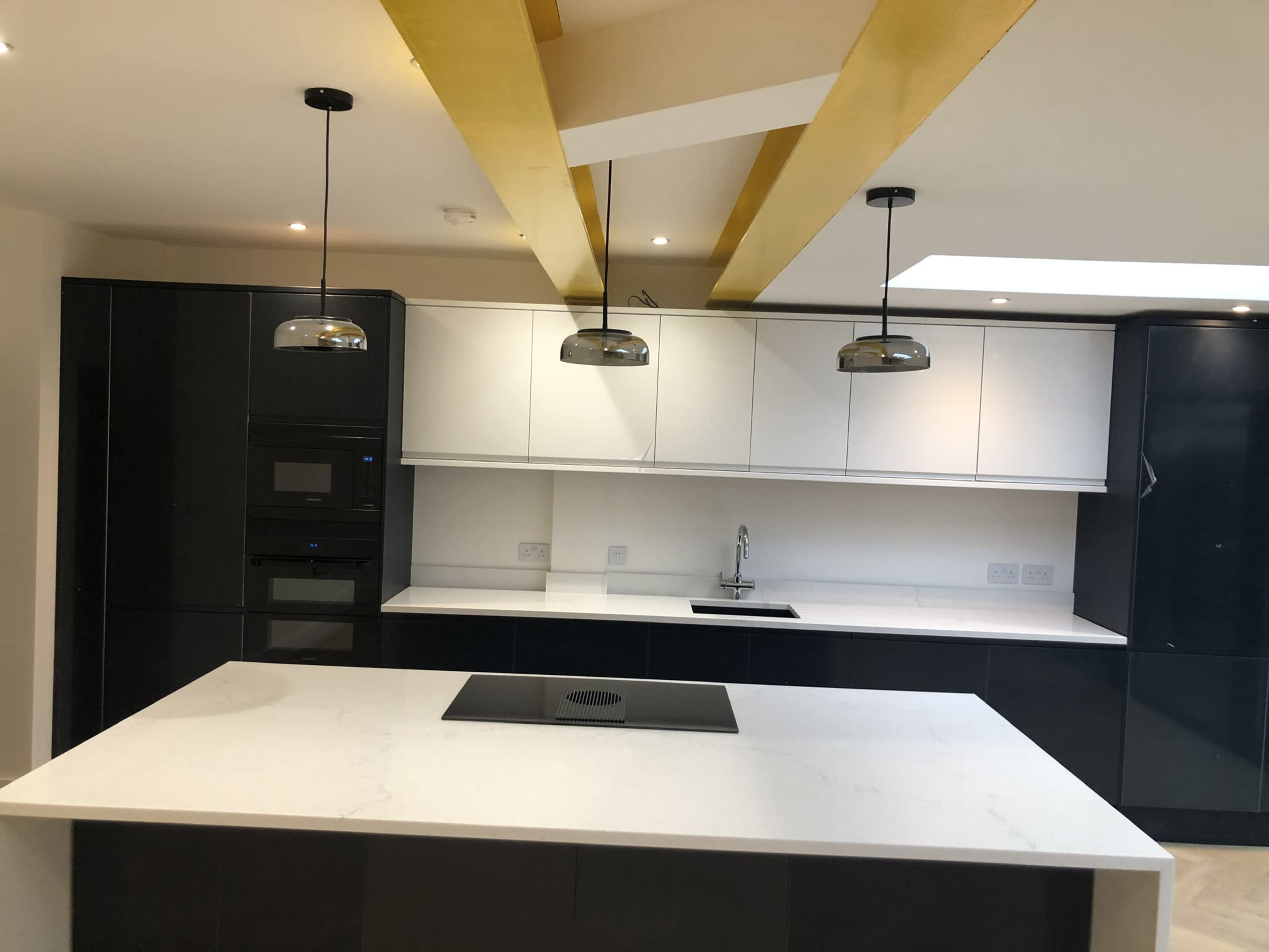 The kitchen features a central island with a built-in cooktop, complementing sleek black and white cabinetry and pendant lighting.
