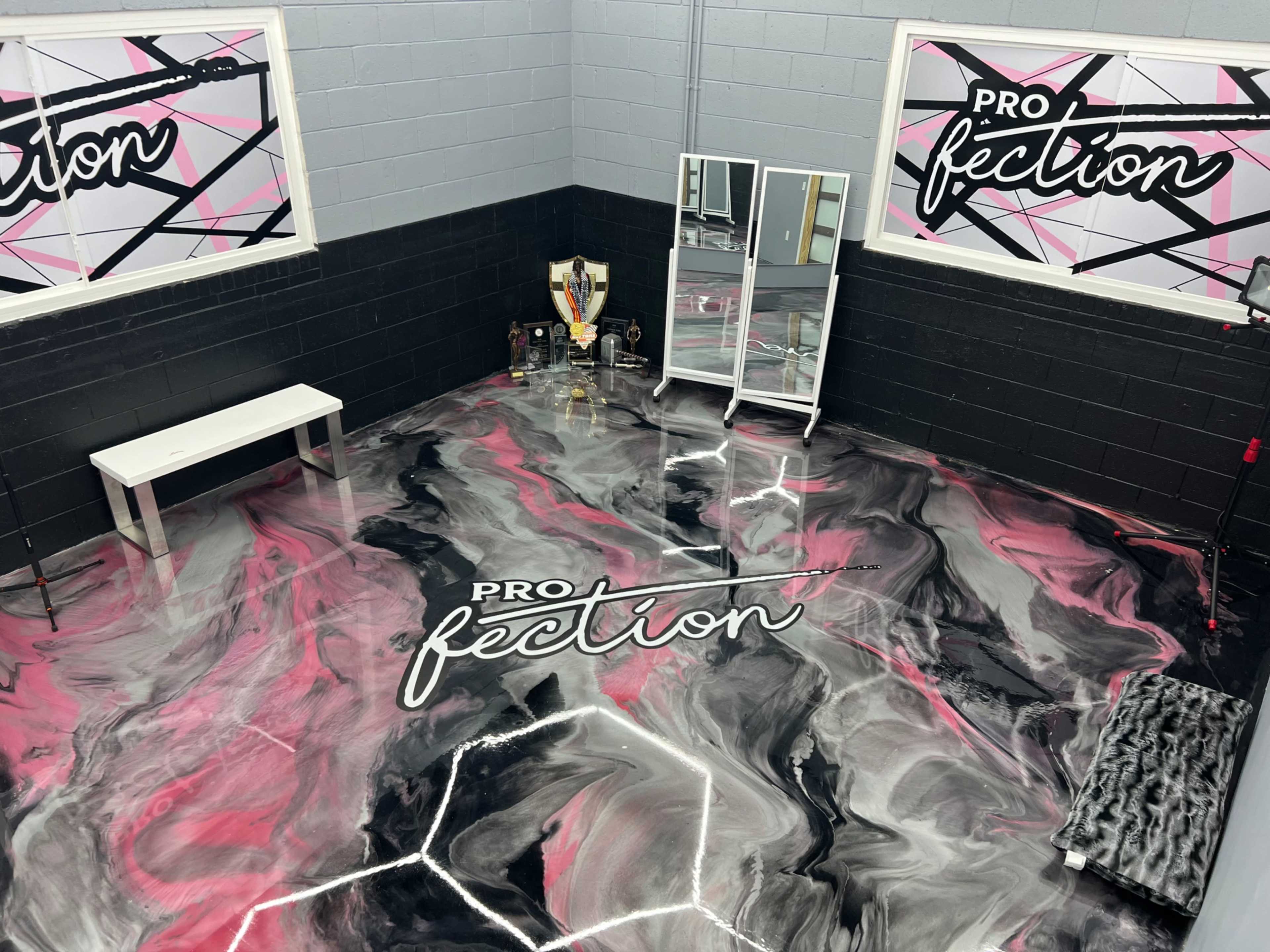 The image shows a corner of a room with a patterned black and pink floor, a white bench, a mirror, and various objects displayed on shelves.