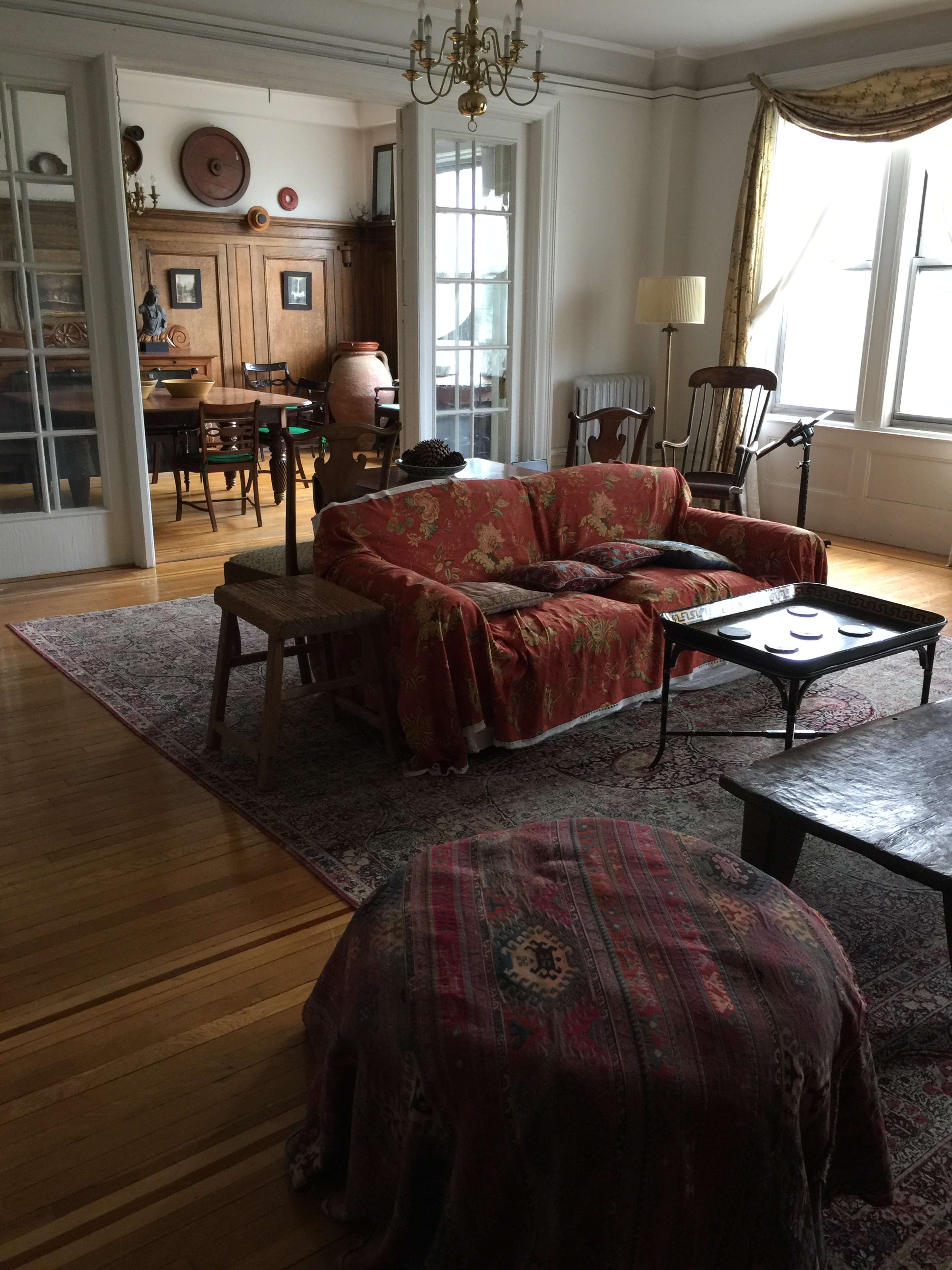 The room features a cozy living area with a sofa draped in a patterned cover, a coffee table, and a visible dining space in the background.