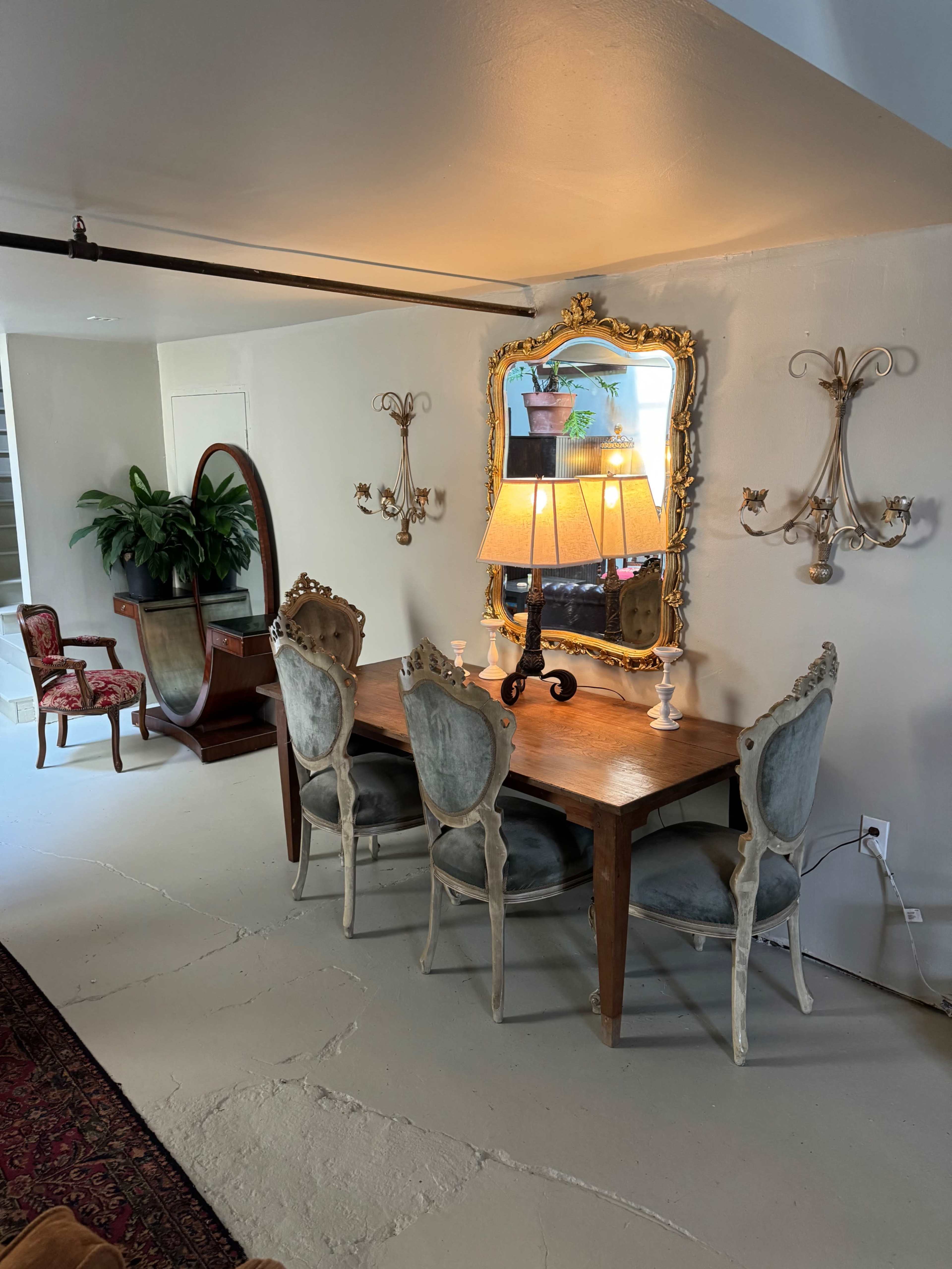 A dining area with a wooden table and four upholstered chairs, accompanied by a mirror and wall-mounted sconces.