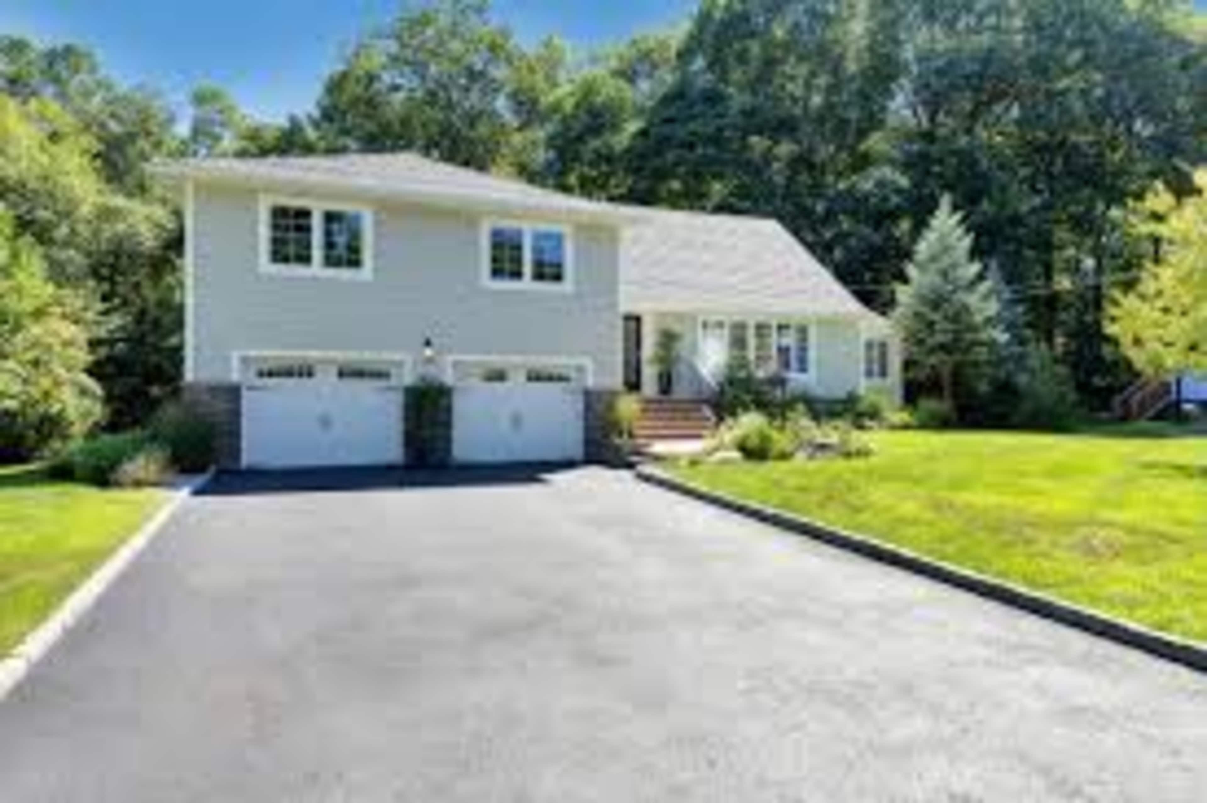 A two-story house with a sloped roof and a double garage is situated on a well-maintained lawn surrounded by trees.