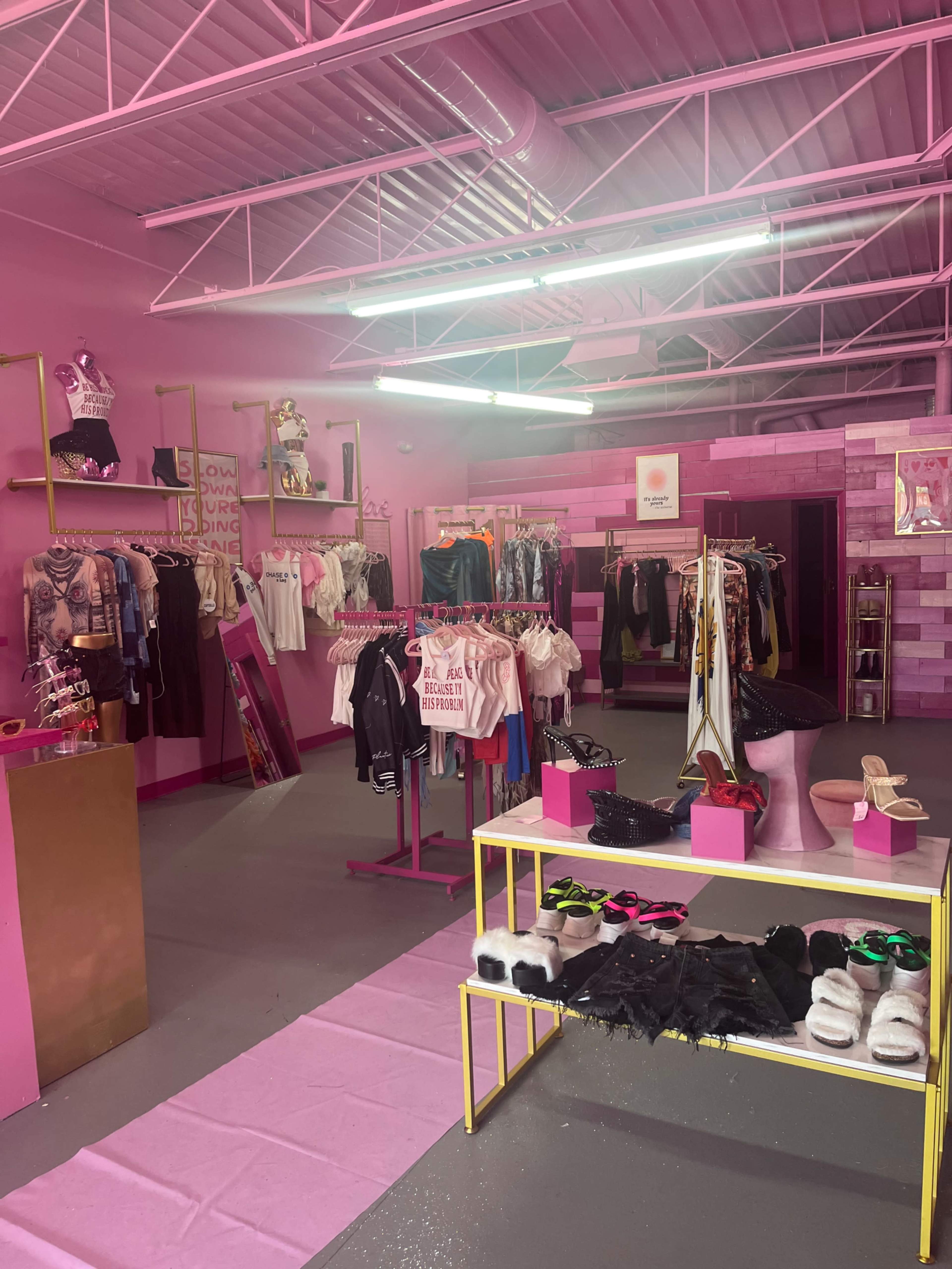 The image depicts a clothing store interior featuring pink walls, racks of apparel, and displays of shoes and accessories.