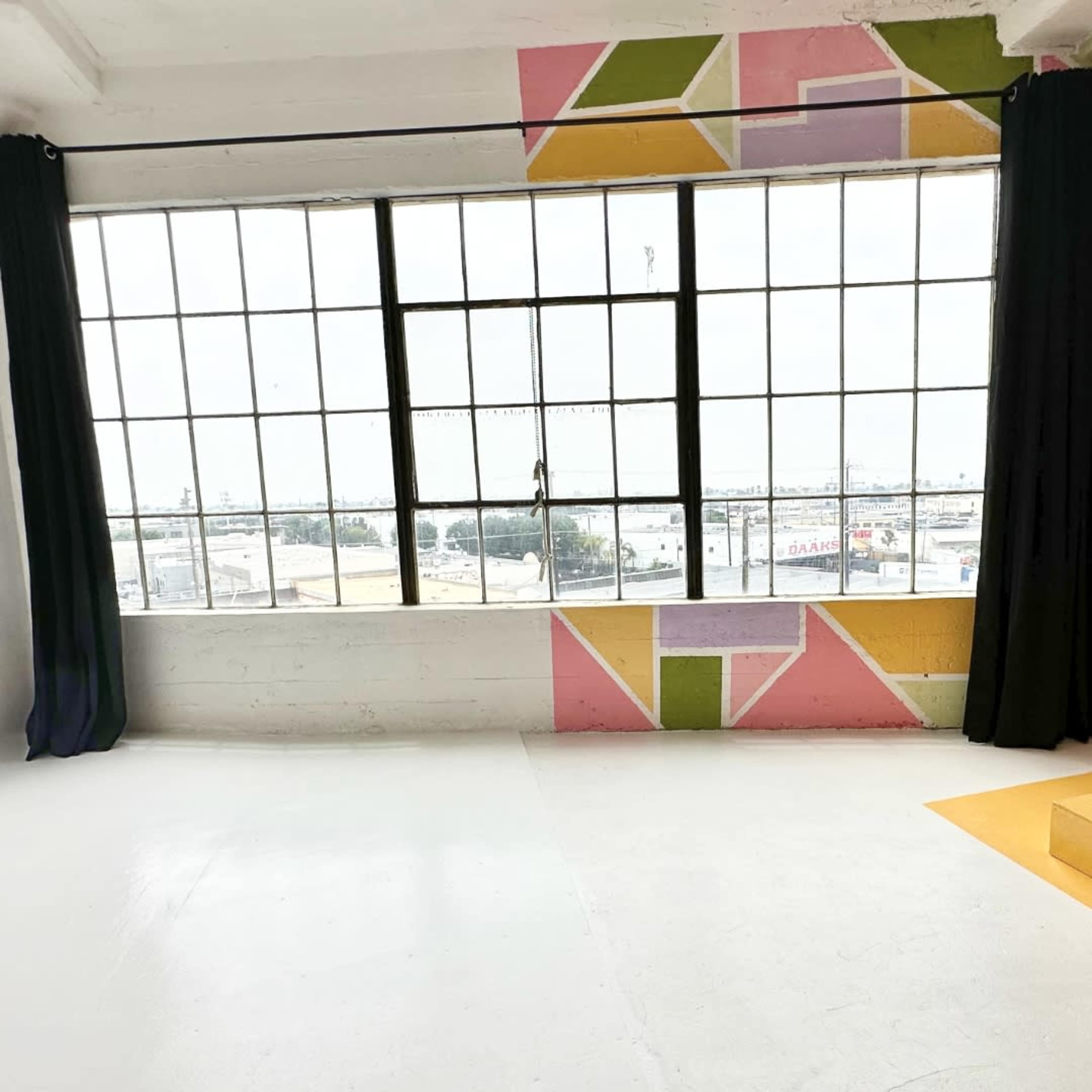 An empty room with large industrial windows and colorful geometric wall murals.