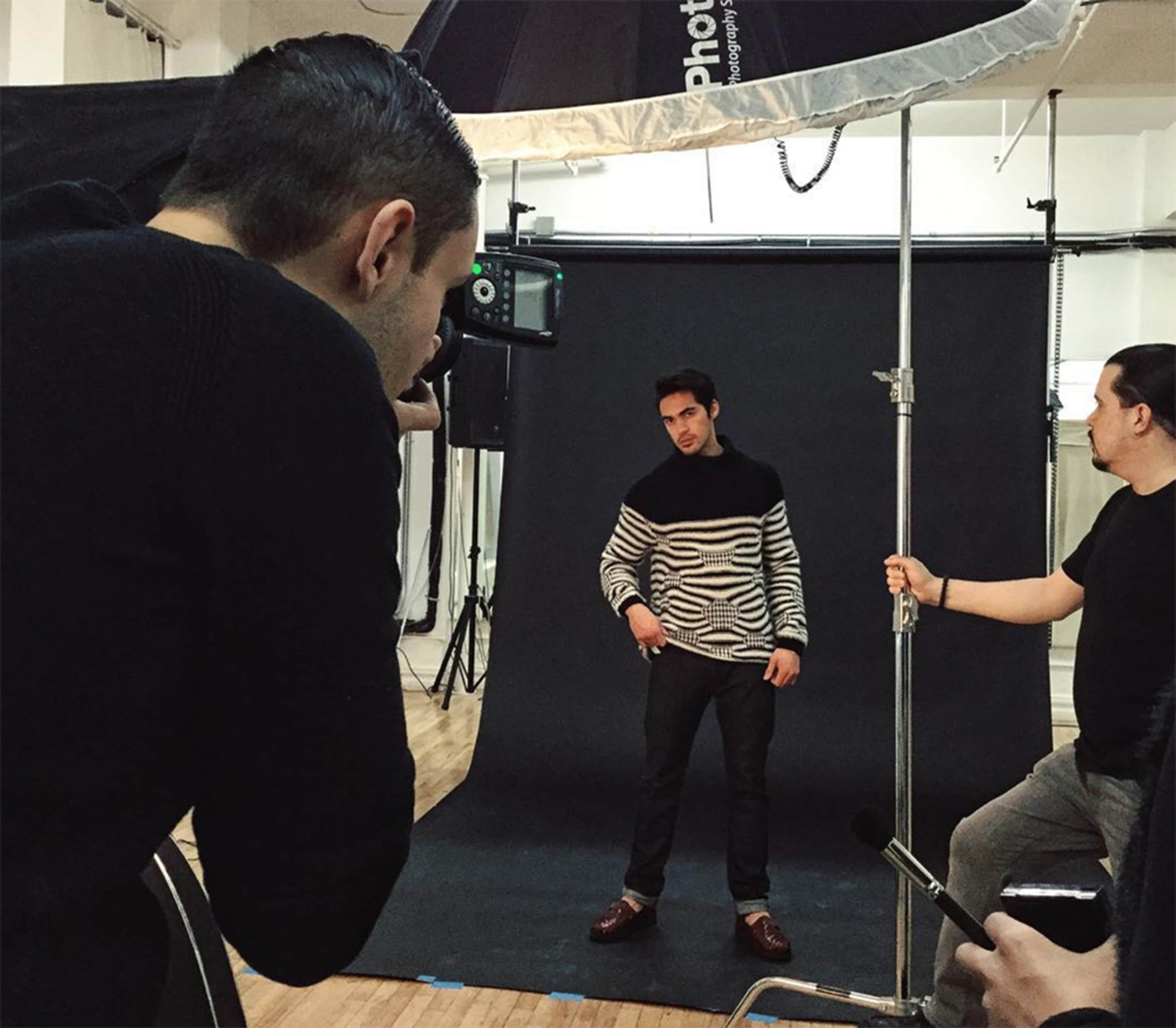 A photographer is capturing a model posing against a black backdrop in a studio setting.