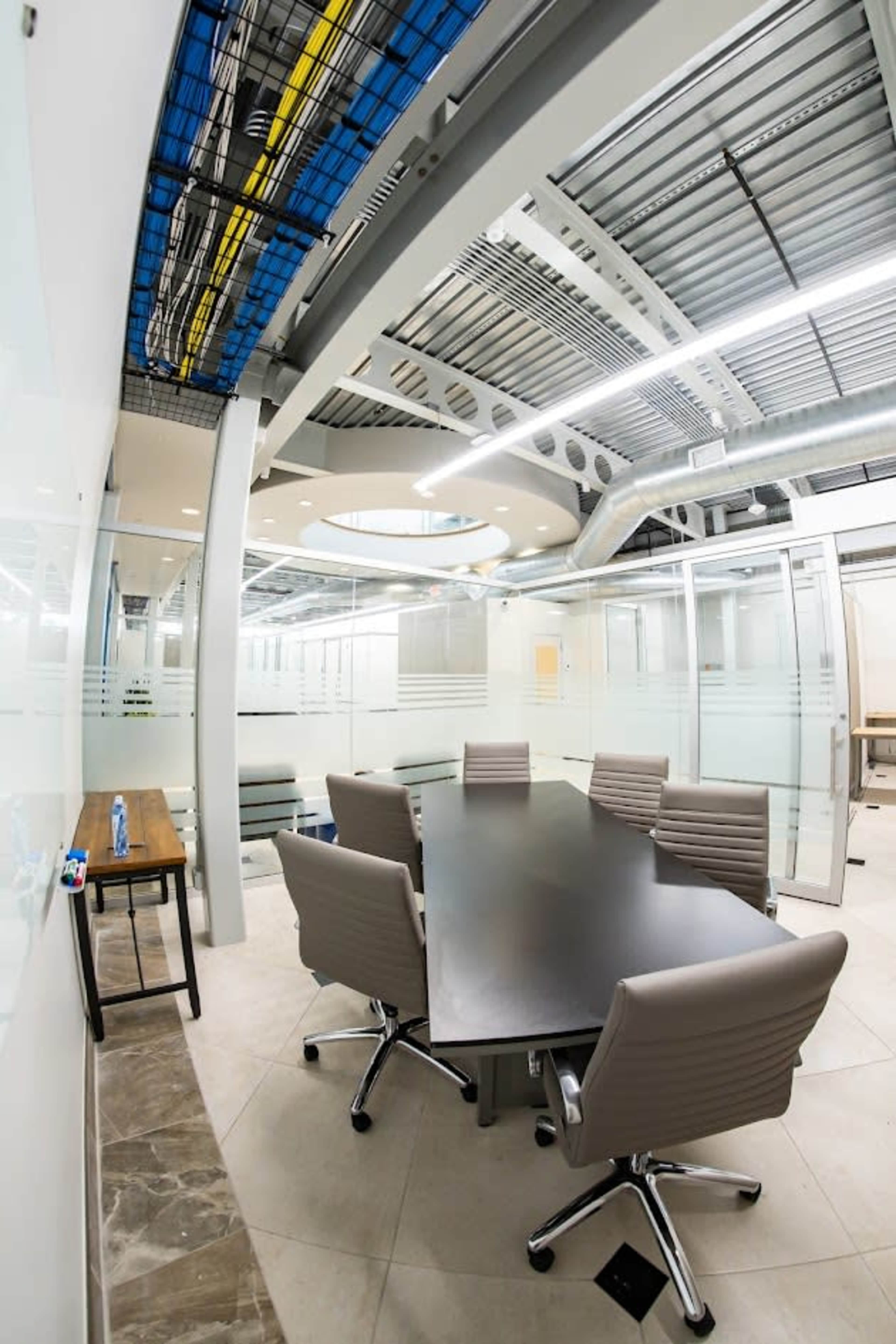 The image shows a modern conference room with a large black table surrounded by six chairs and glass walls.