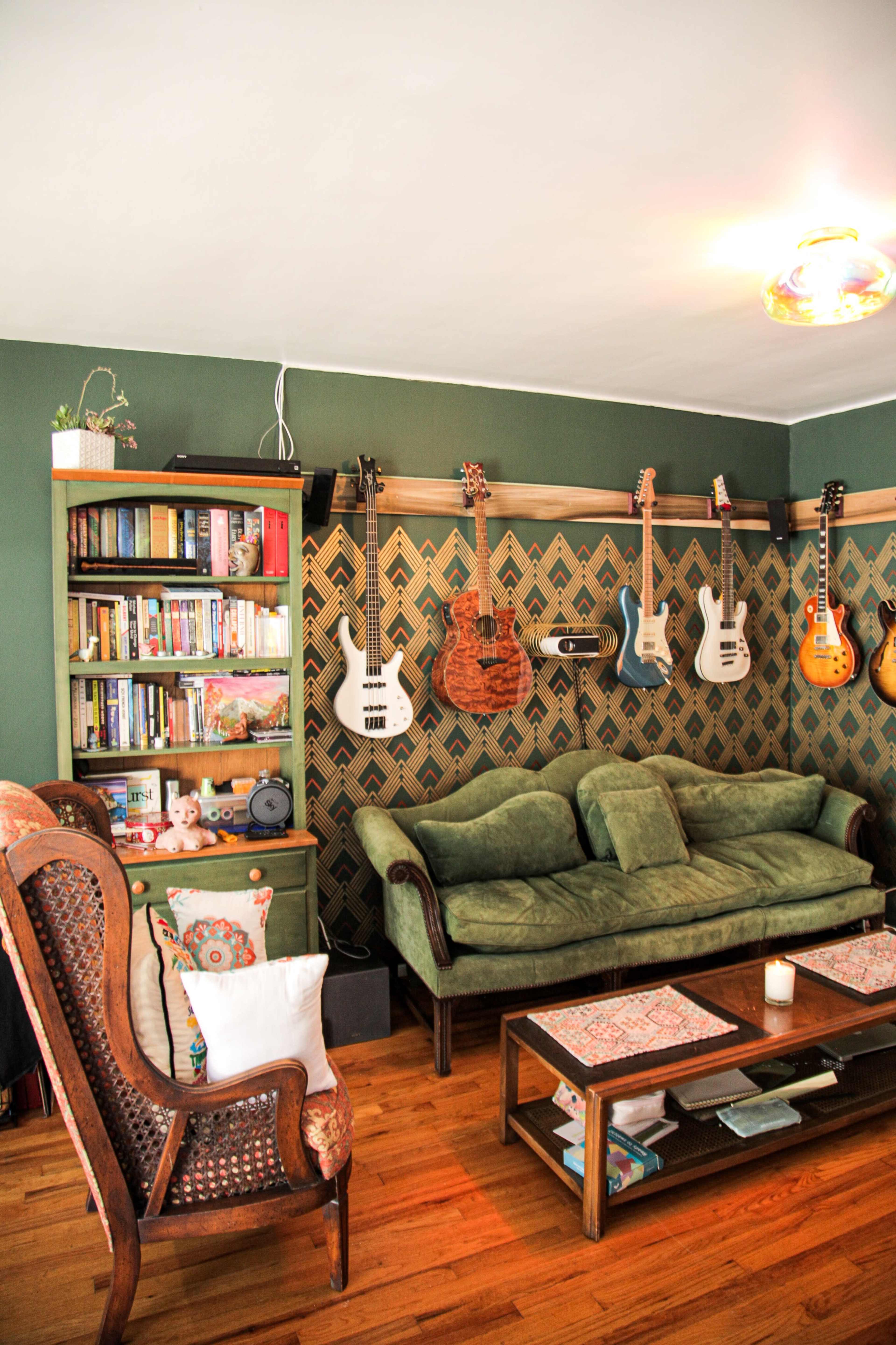 A cozy living room with green walls, a bookshelf filled with books, a green sofa, and several guitars displayed on the wall.