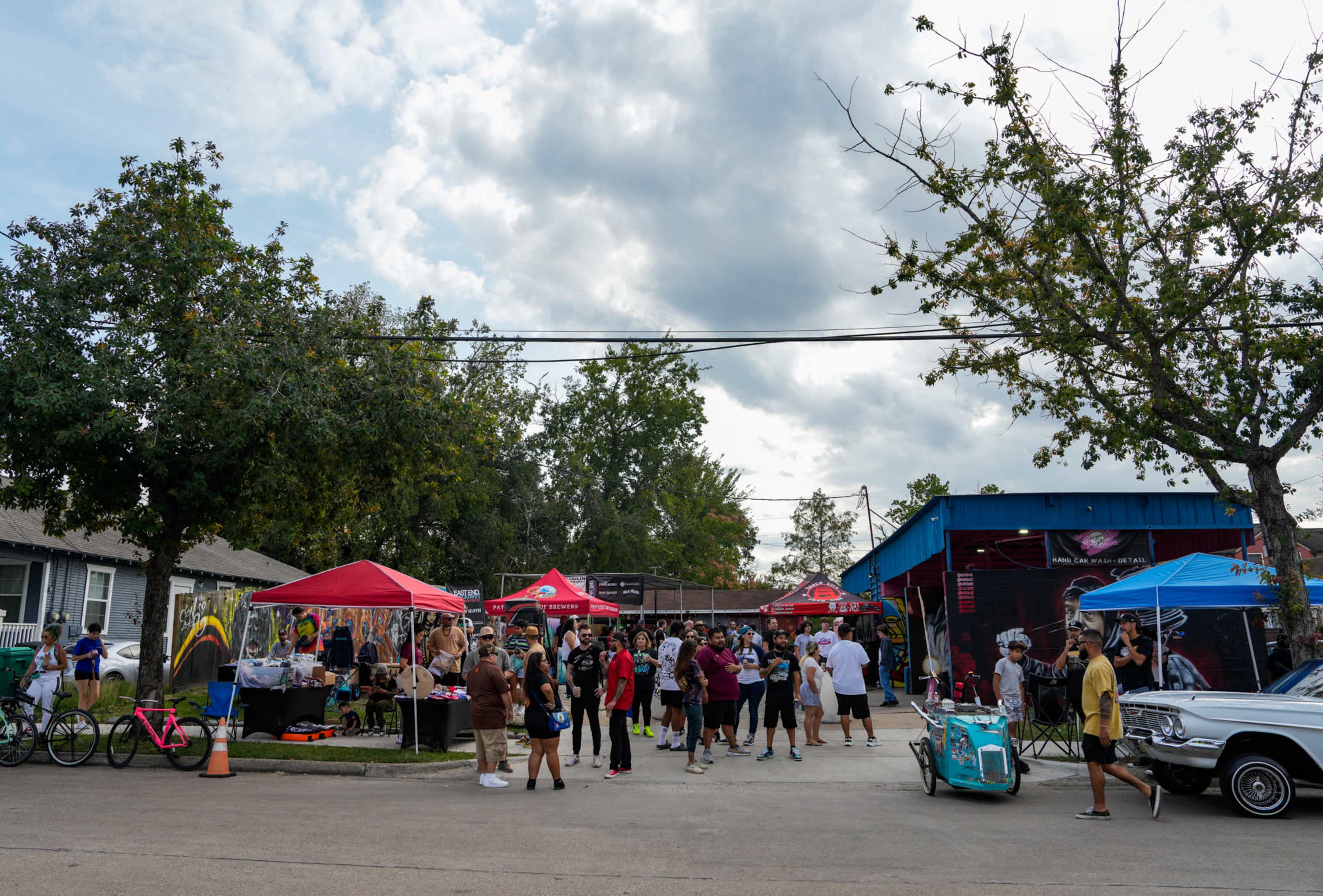 A crowd gathers at an outdoor event with tents and activities in front of a building under a cloudy sky.