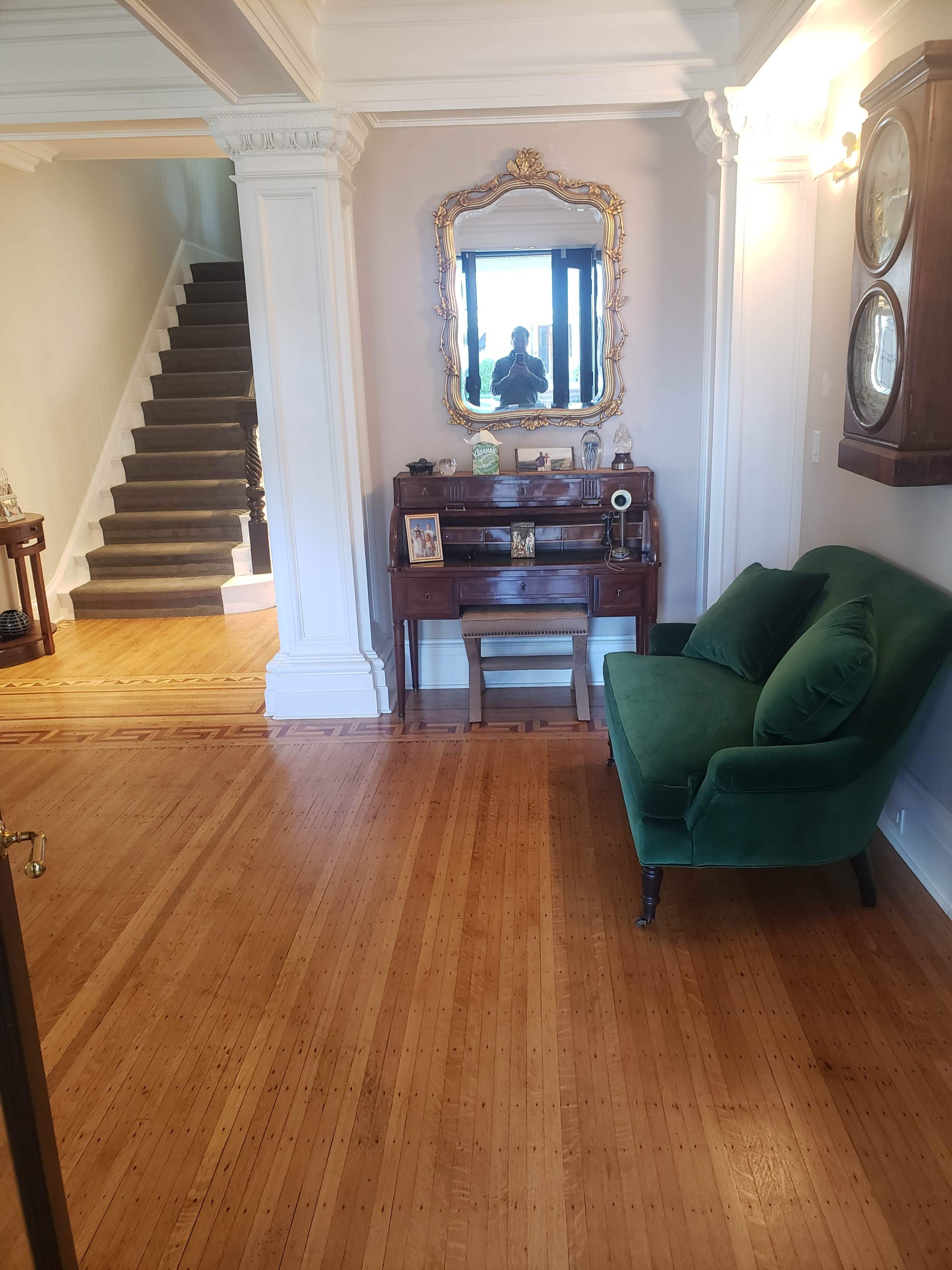 The image shows a well-lit hallway featuring a green couch, a console table with decorative items, and a staircase in the background.
