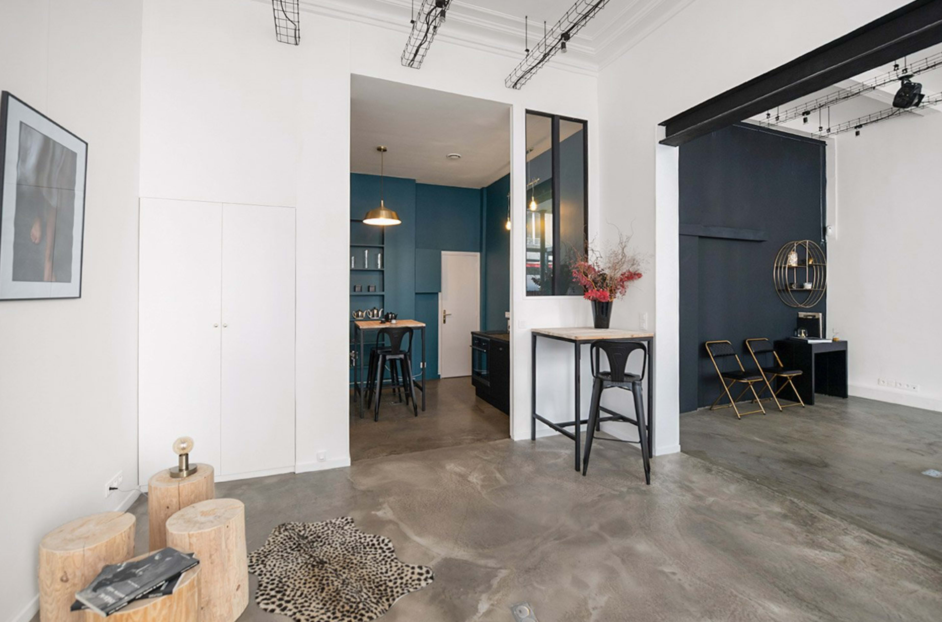 A modern open living space featuring a kitchen area, wooden stools, and a mix of decorative elements on the floor.