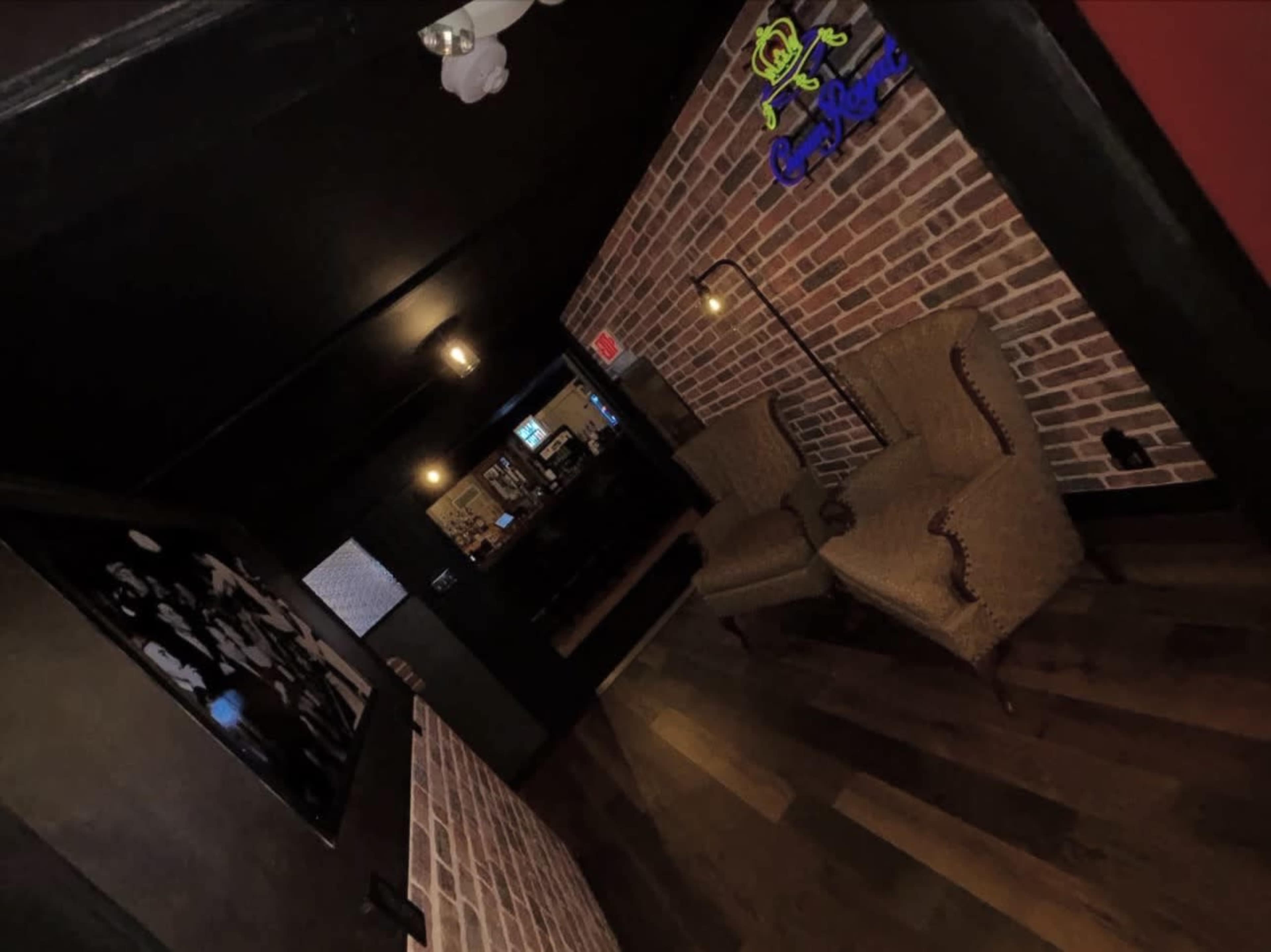 The image shows a narrow hallway with exposed brick walls, wooden flooring, and two patterned armchairs facing each other.