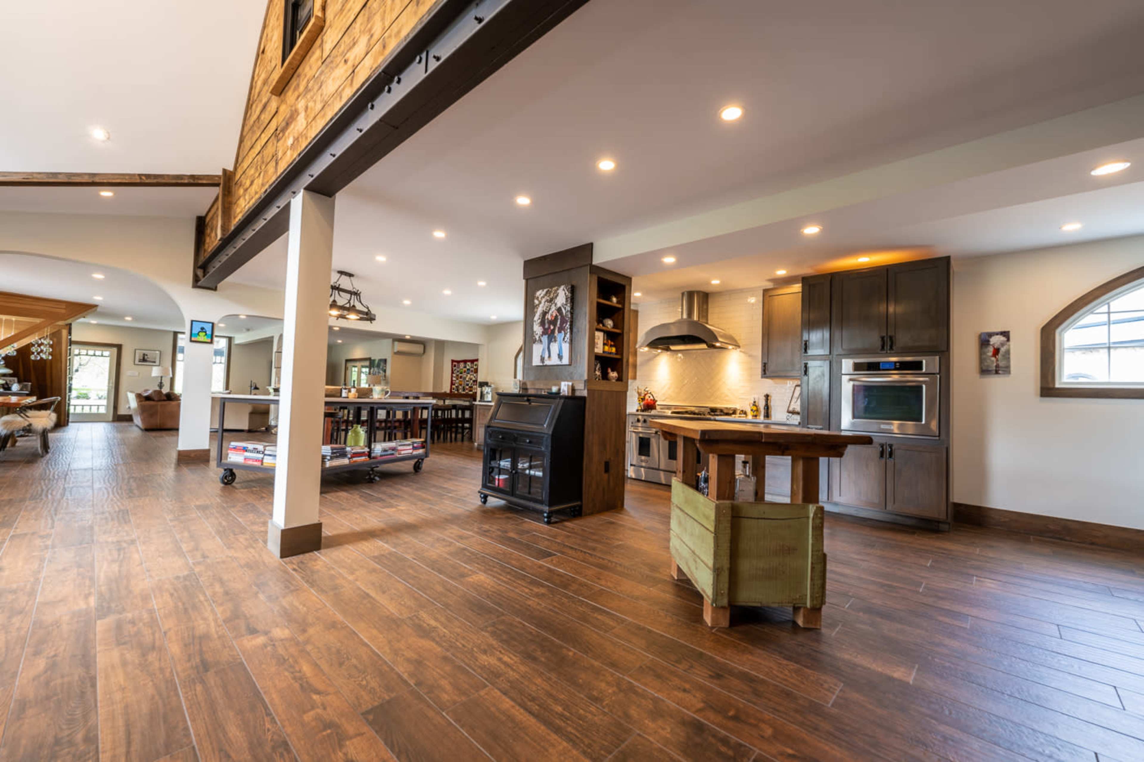 A spacious, modern kitchen with wooden floors, a central island, and various appliances, leading to an open living area.