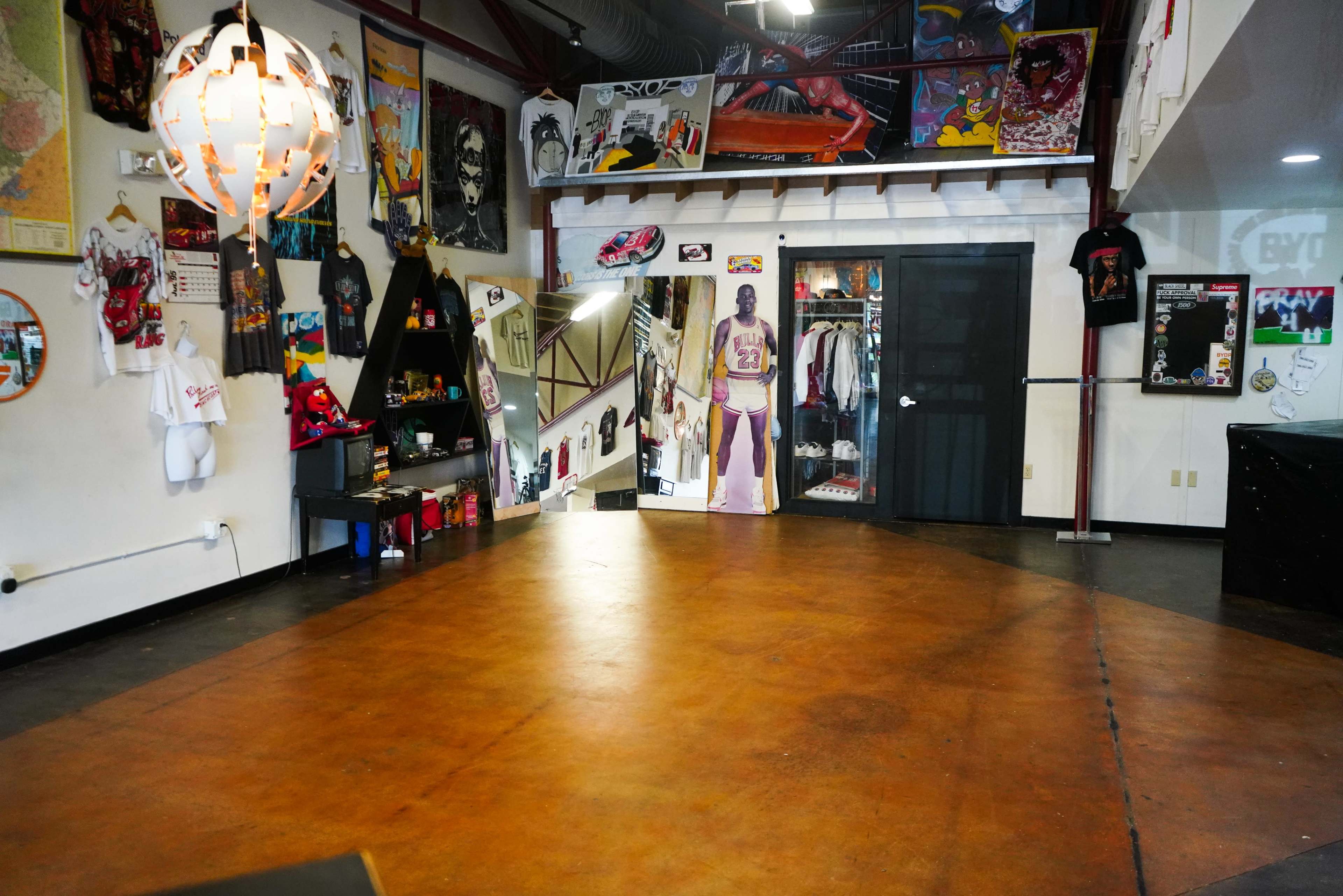 A spacious interior featuring a wooden floor, walls adorned with various artworks, and a mirrored door leading to a clothing area.