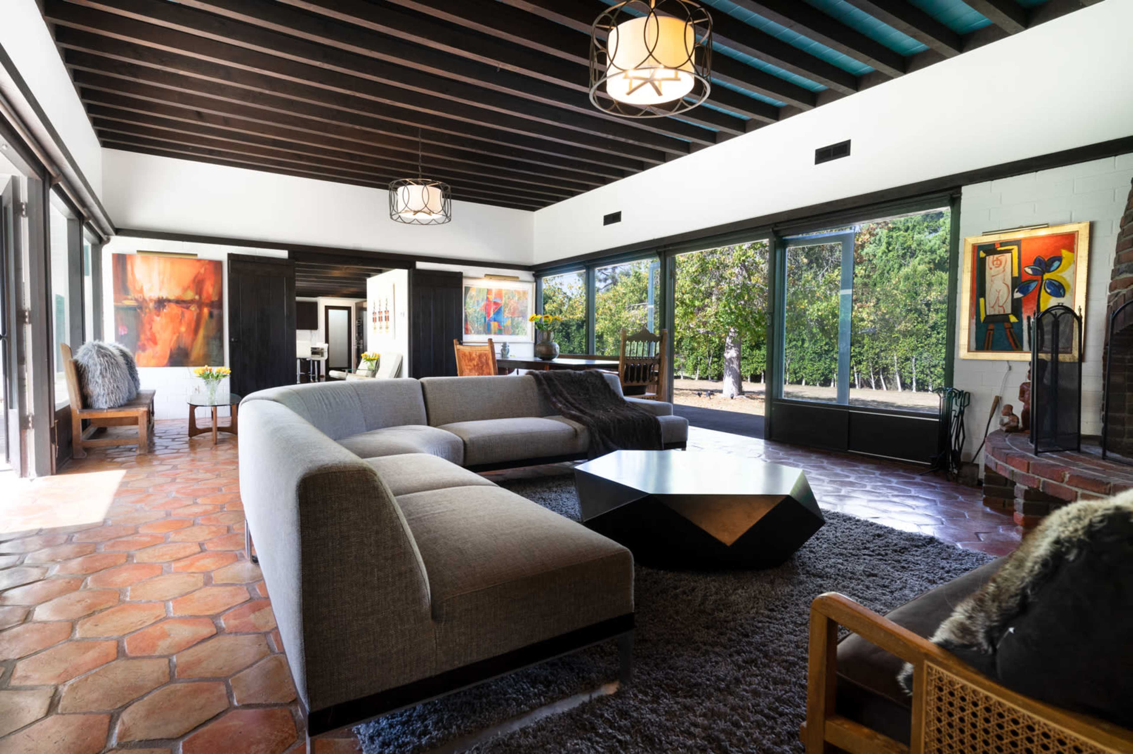 A spacious living room with a large sectional sofa, a geometric coffee table, and large windows that open to a view of greenery outside.