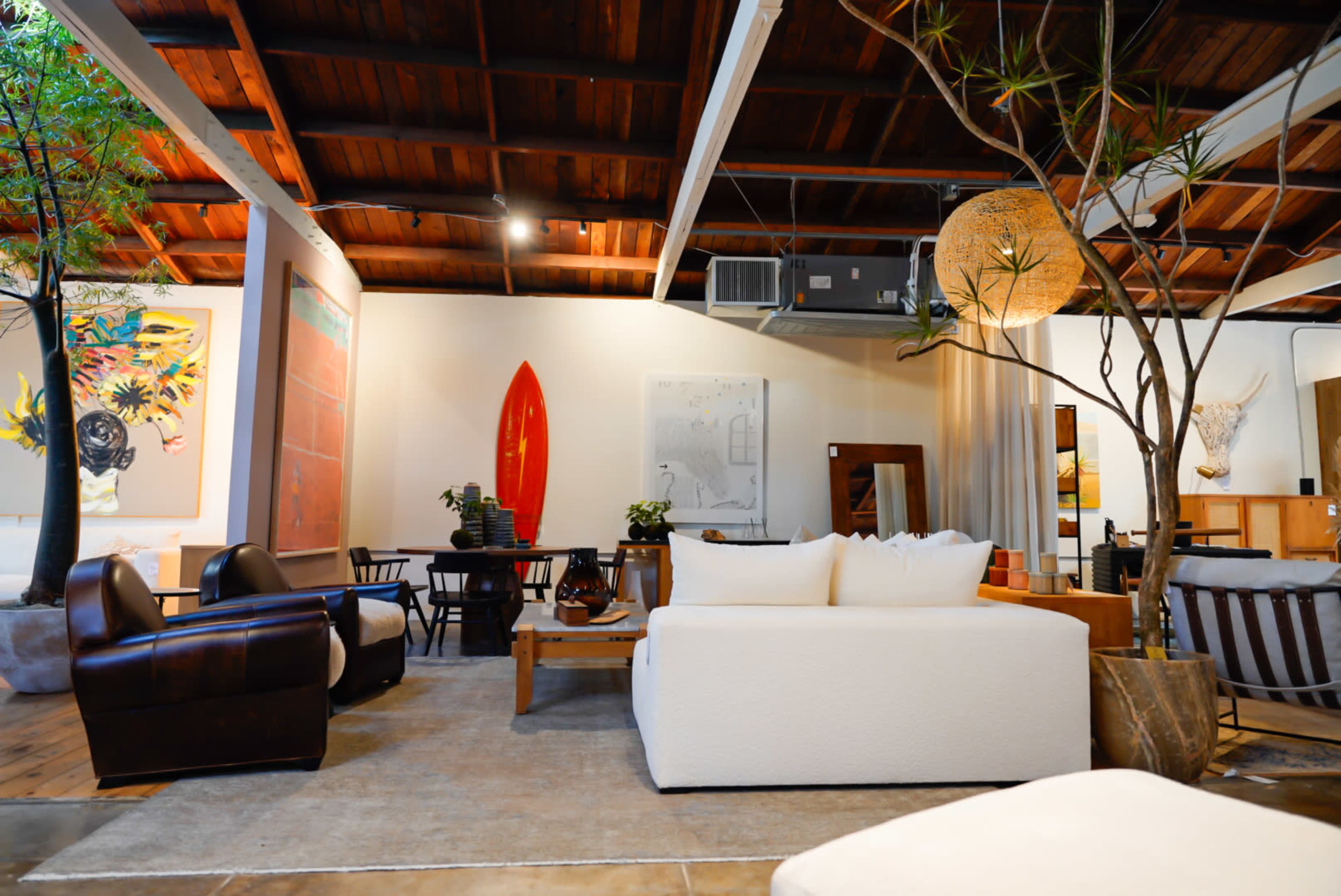 The image shows a stylish interior living space featuring a mix of modern furniture, decorative plants, and artwork on the walls.