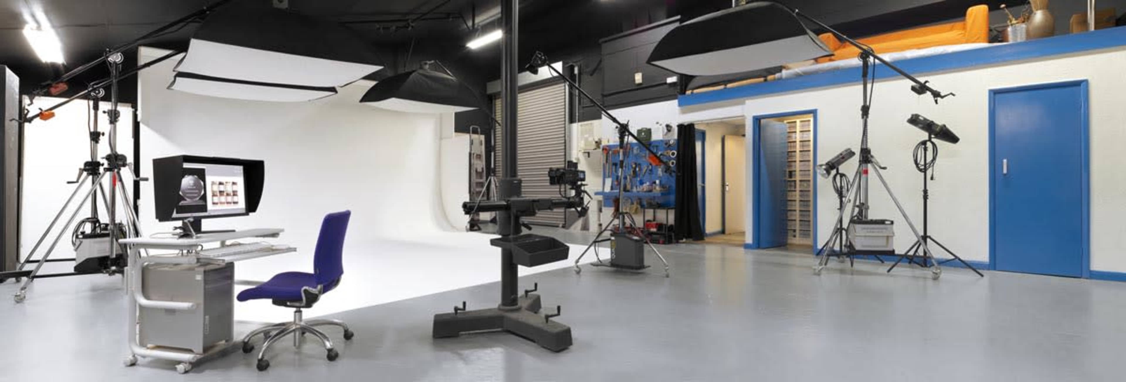 A photography studio equipped with lighting setups, a computer workstation, and various photography equipment against a white backdrop.