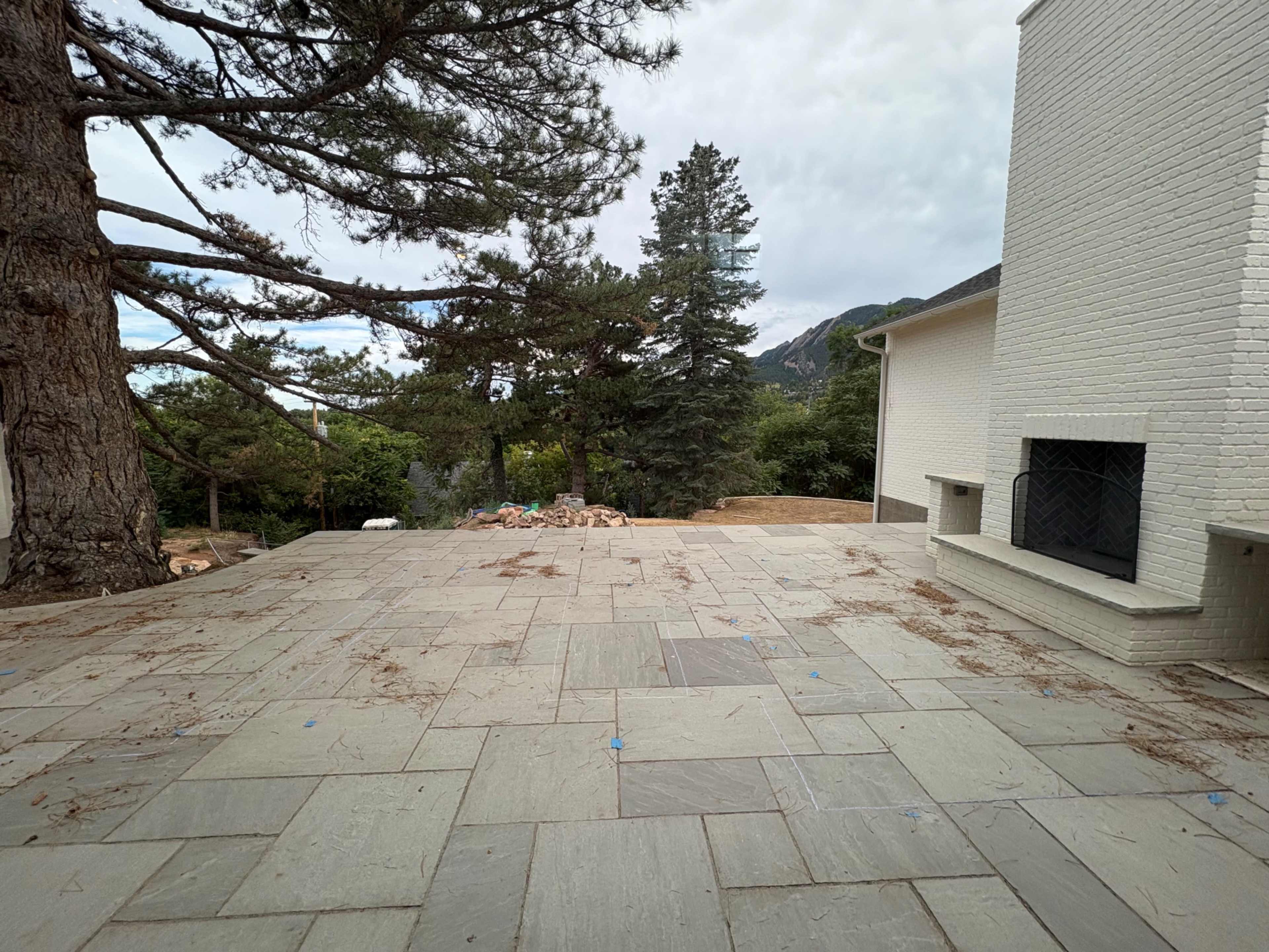 The image shows a stone patio with scattered debris and a view of trees and mountains in the background.