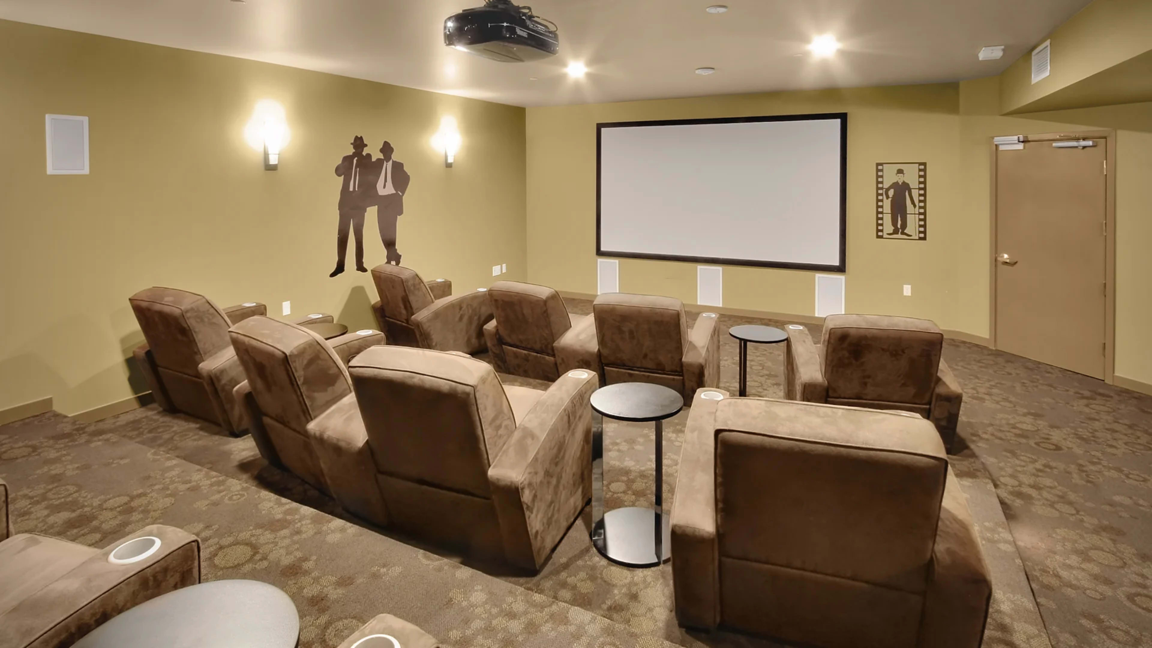 A small home theater room with plush seating, a large screen, and projector mounted on the ceiling.