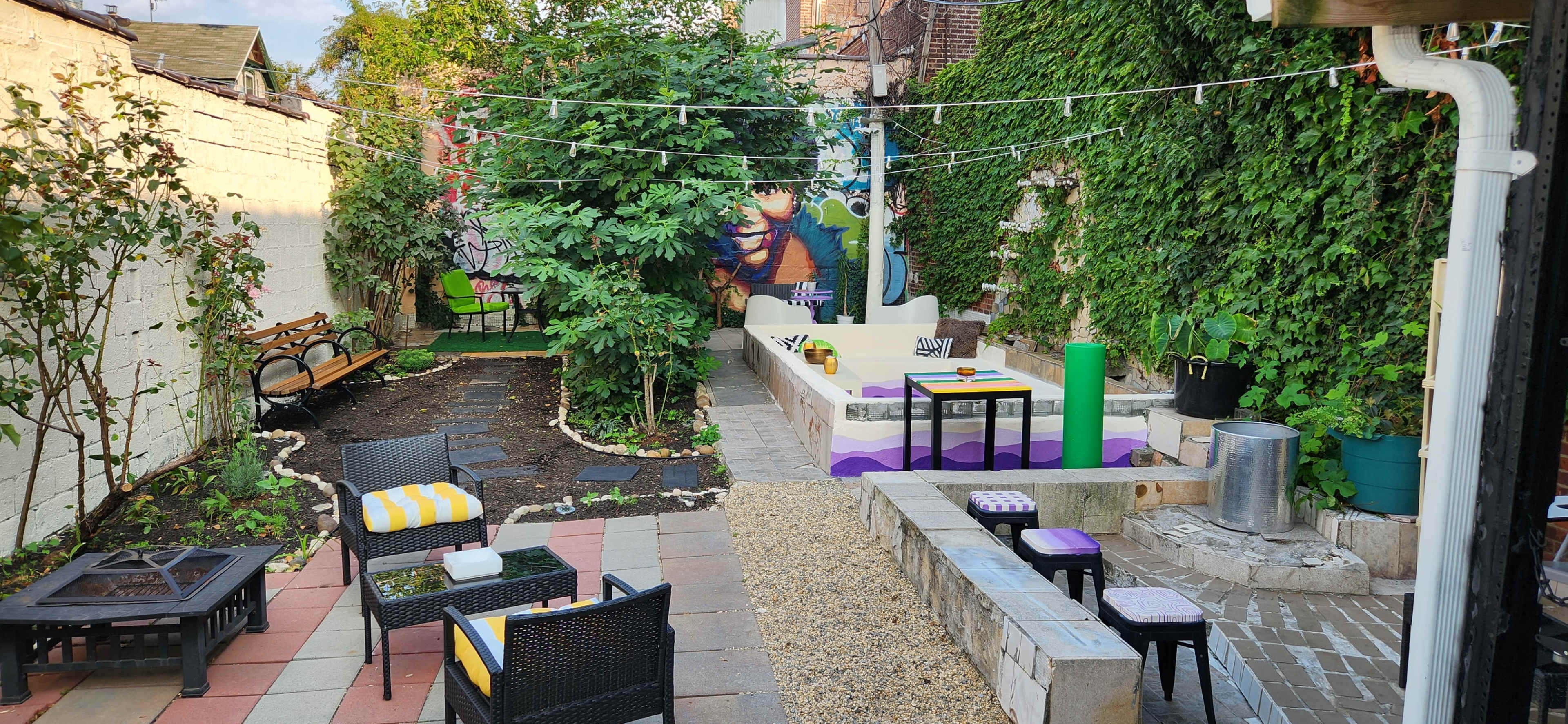 The outdoor space features a garden with seating areas, a fire pit, and colorful murals on the walls.