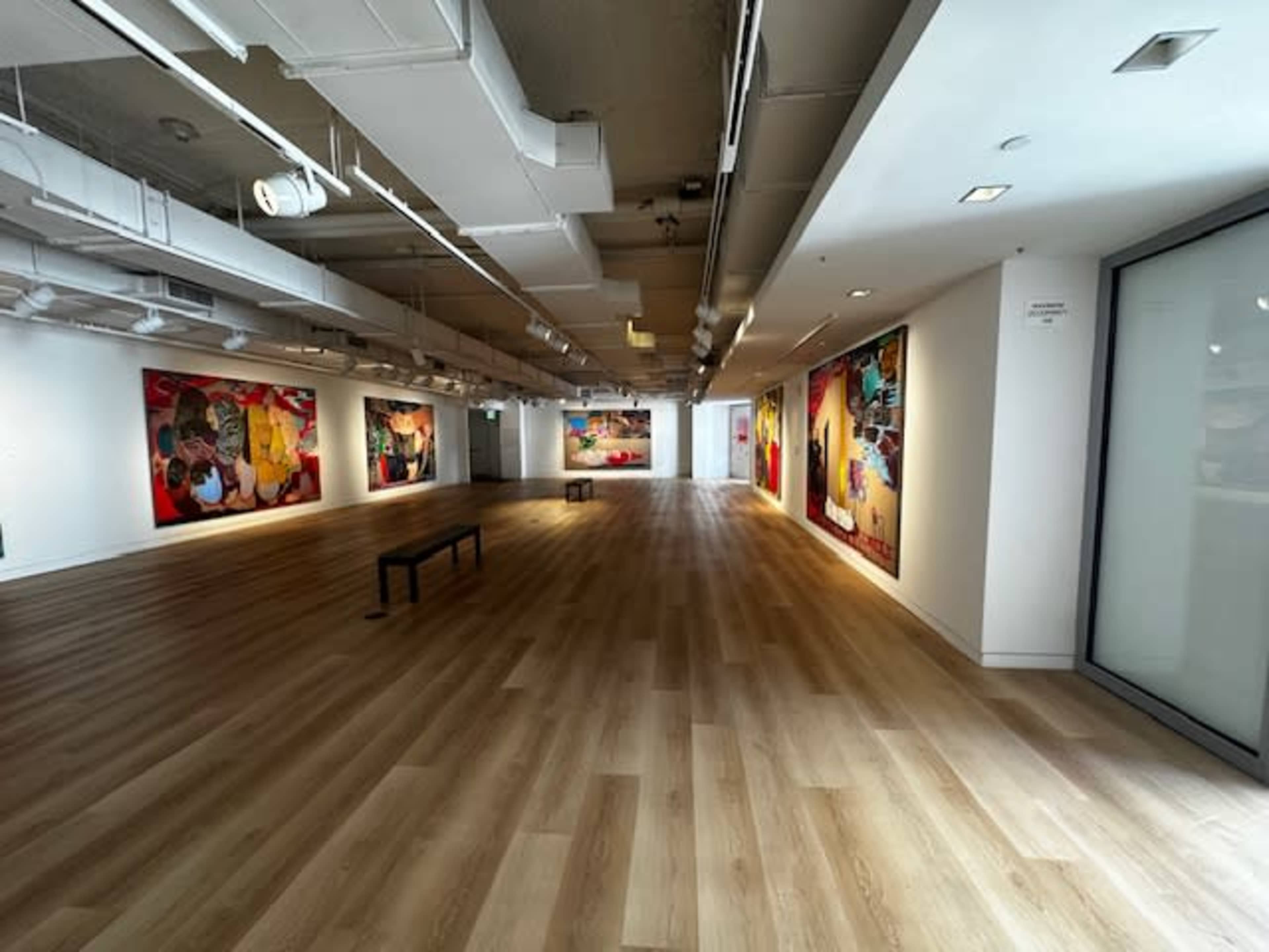 A spacious art gallery with wooden floors and large colorful paintings on the walls.