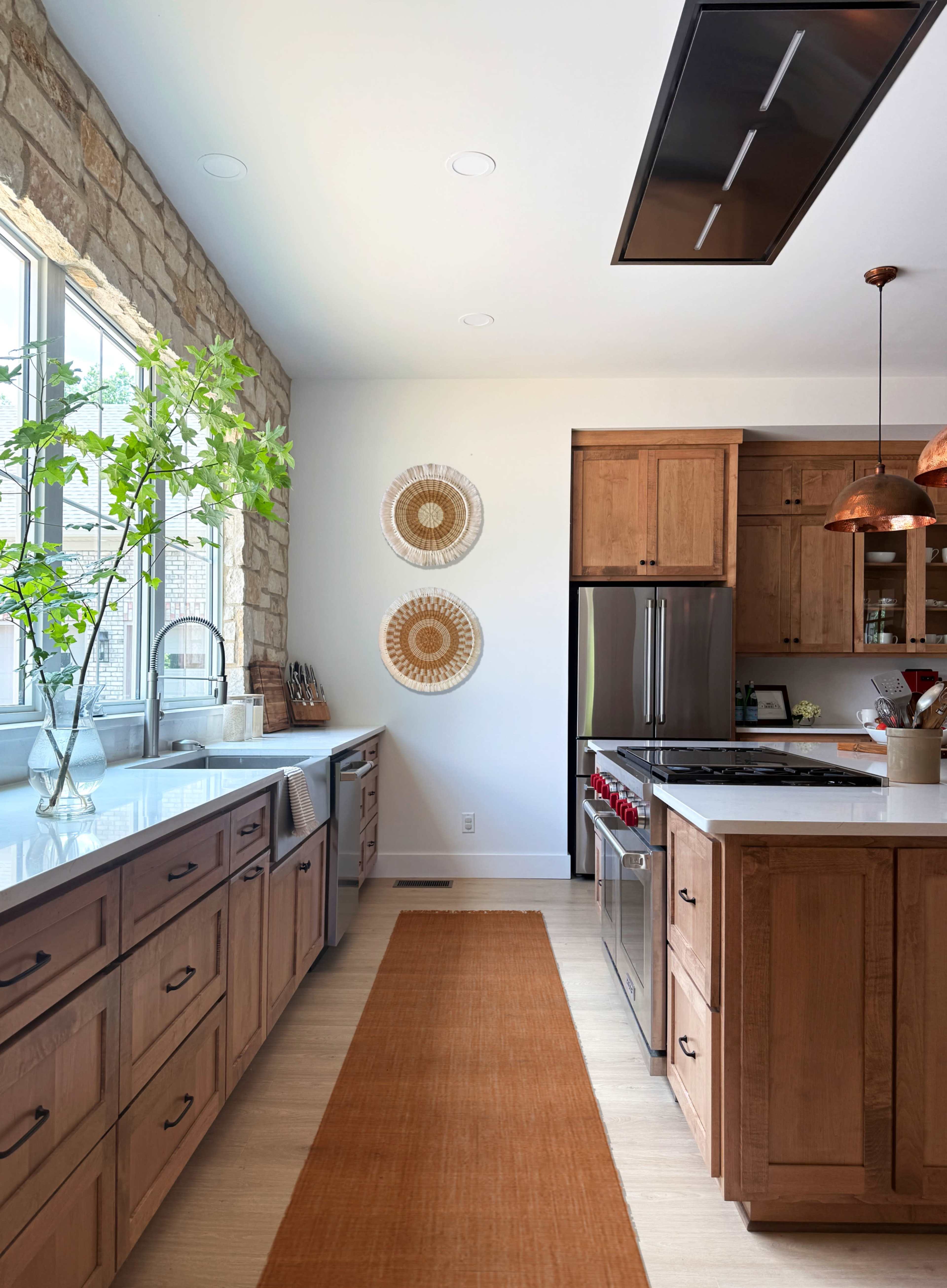 The kitchen features wooden cabinets, a large window with a plant, and a central island with a stovetop, along with decorative wall hangings.