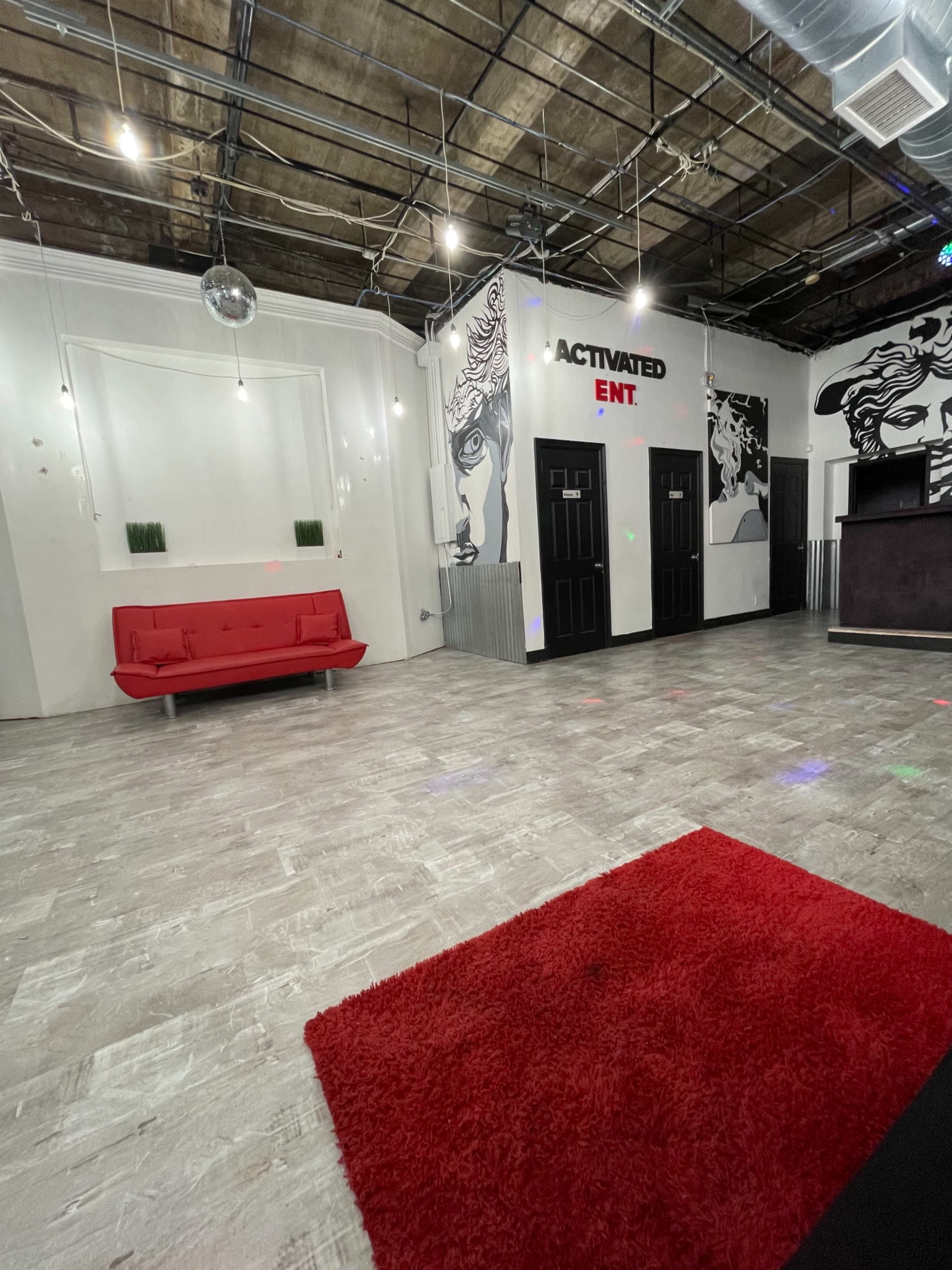 A spacious interior with a red sofa, a red rug, and a front desk area, featuring wall art of faces and a disco ball hanging from the ceiling.