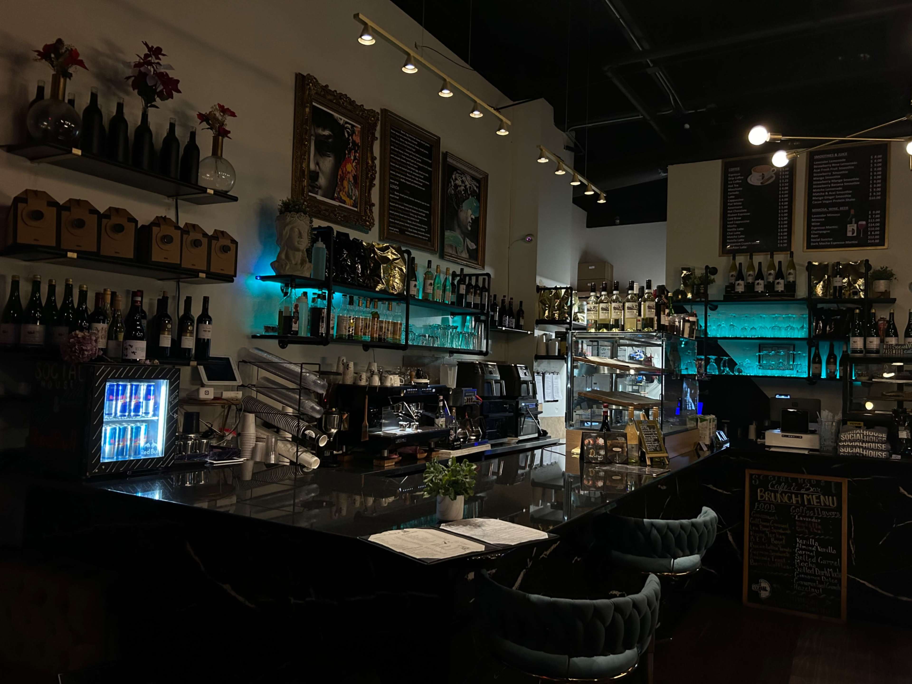 A dimly lit bar with shelves of bottles, a coffee machine, and a counter displaying menus and a chalkboard sign.