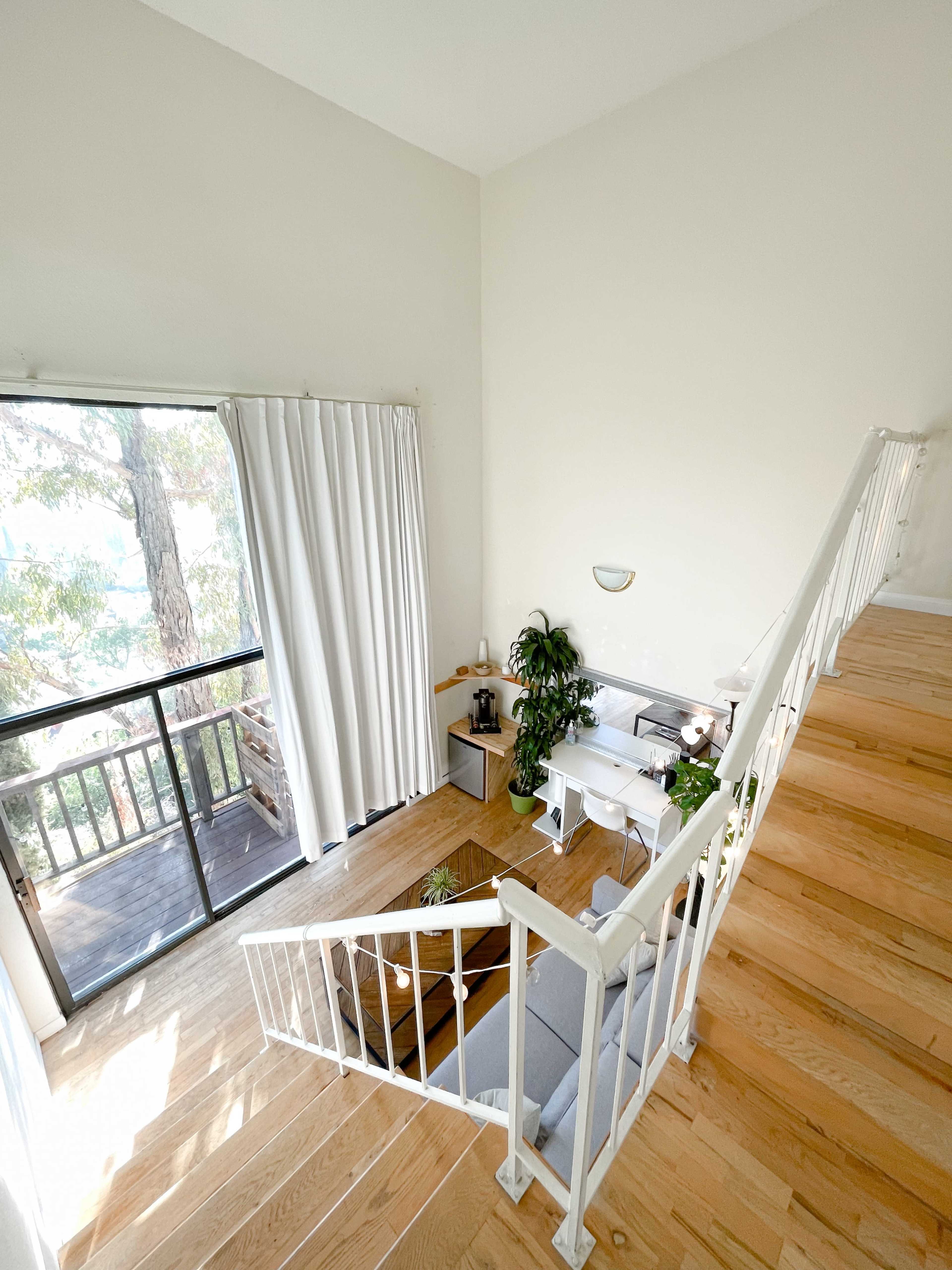 A well-lit staircase leads down to a living area with a large window and indoor plants.