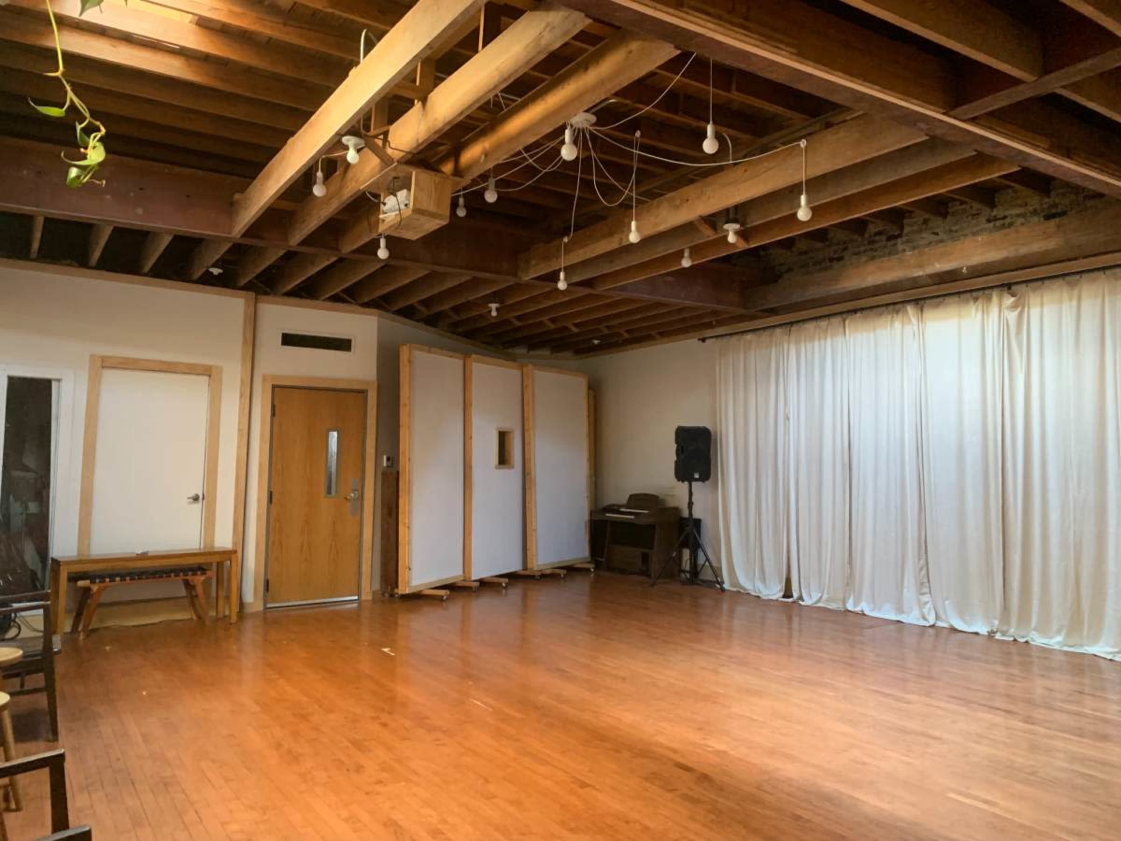 The image shows a spacious, wooden-floored room with exposed beams, curtains on one side, and a folding partition in the center.
