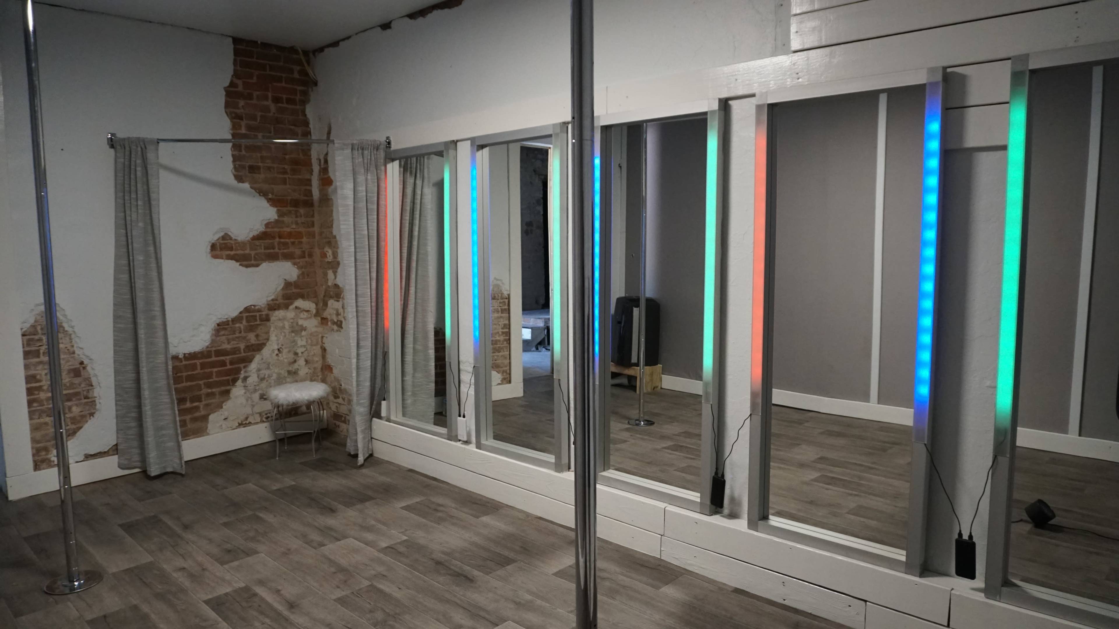 A spacious room features a pole, large mirrors with illuminated edges, and a partially exposed brick wall.