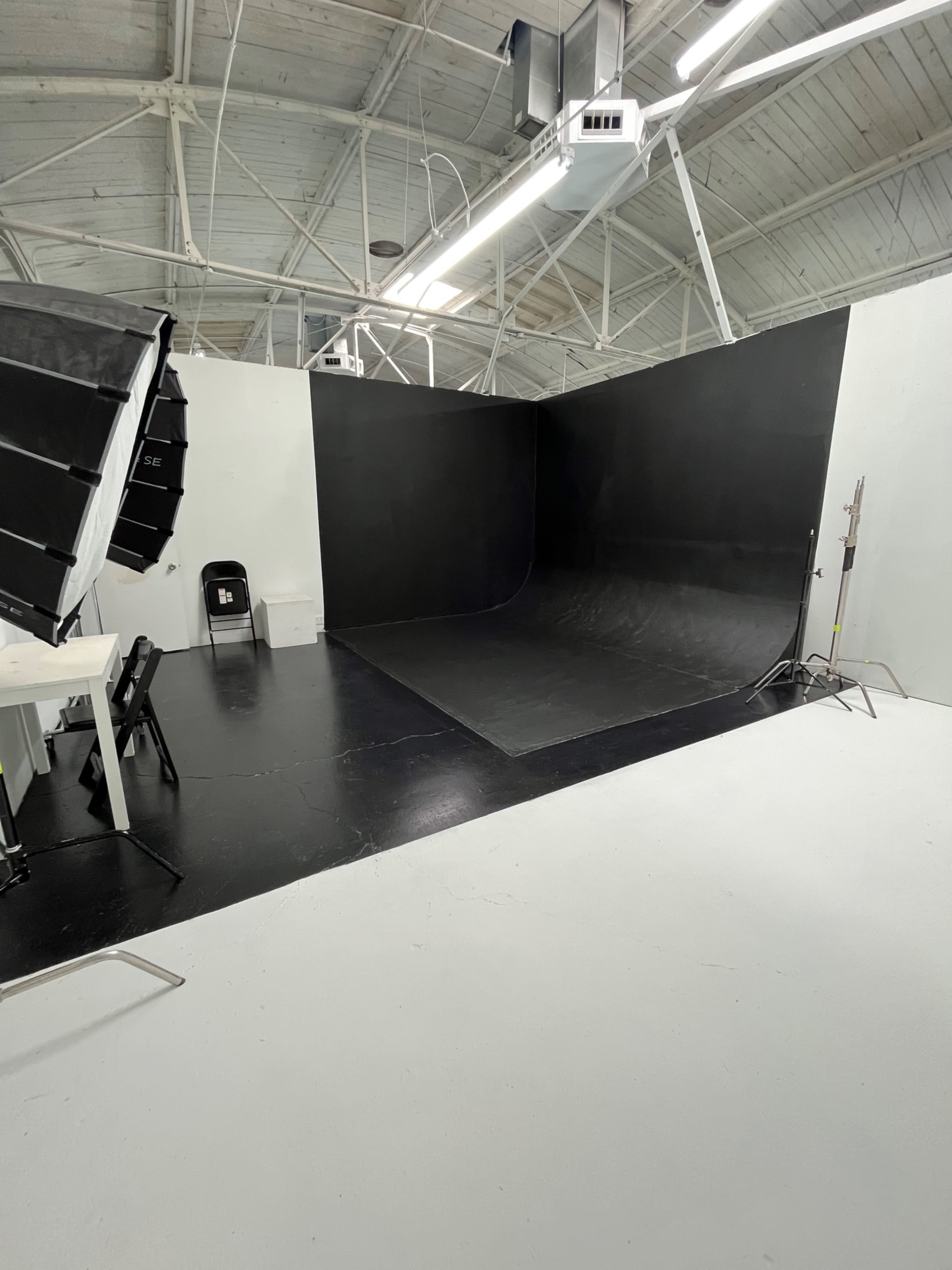The image shows a photo studio with a black backdrop, white walls, and various lighting equipment.