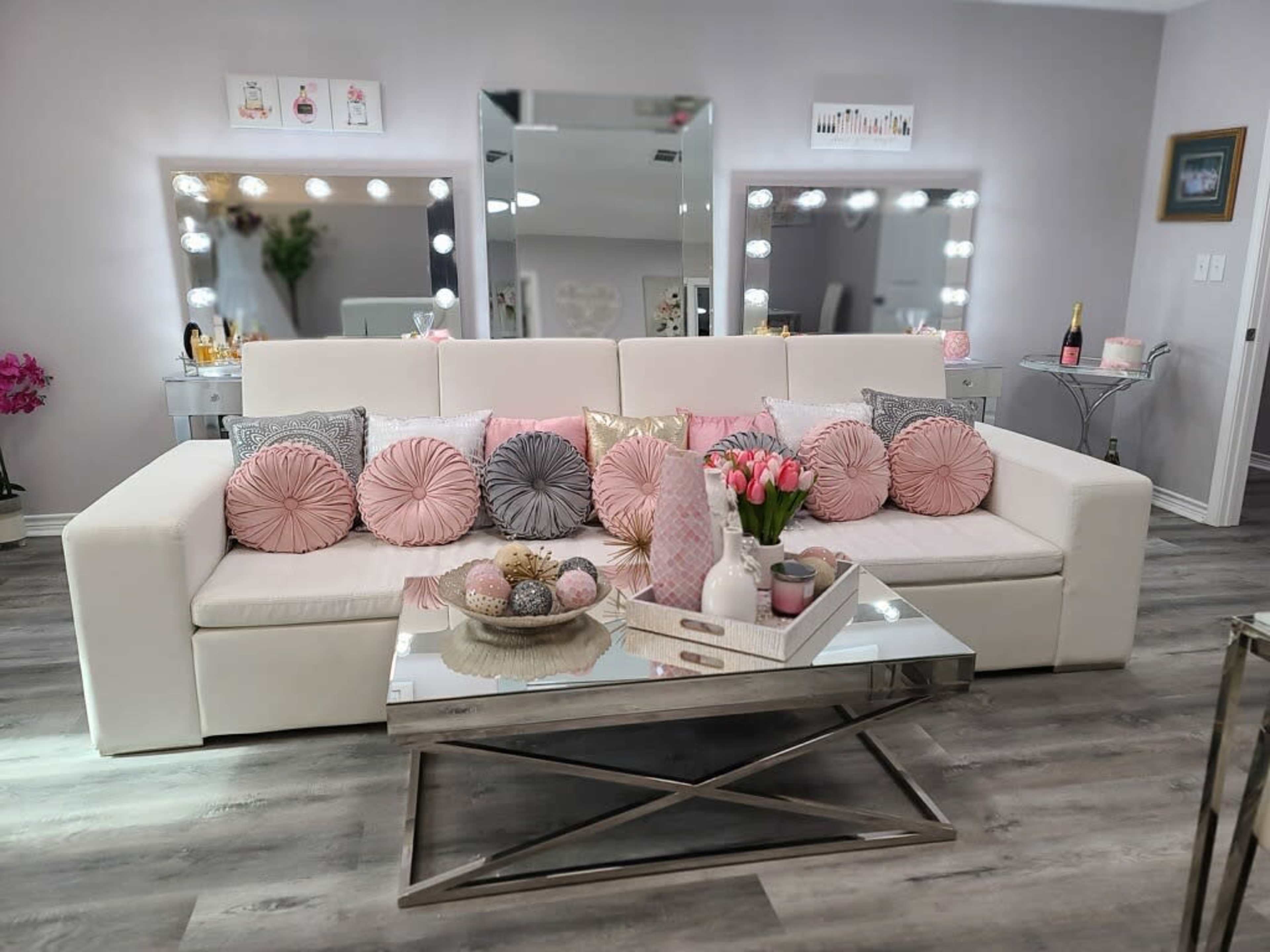 A modern living room with a white sofa adorned with decorative pillows, a glass coffee table in front, and mirrors reflecting the space.