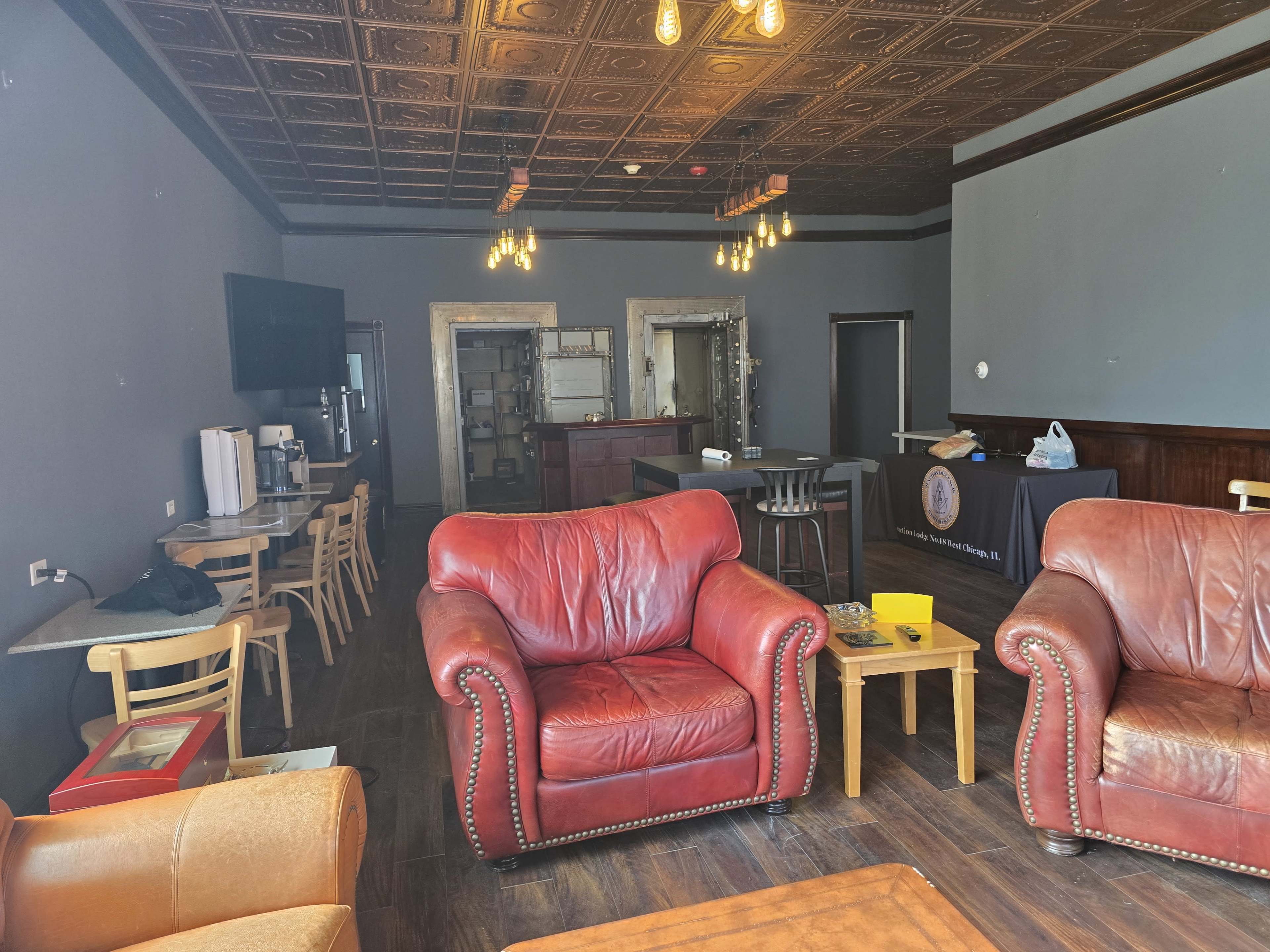 The image shows a spacious café interior with red leather couches, wooden tables, and a bar area in the background, featuring two doorways and a flat-screen TV on the left wall.
