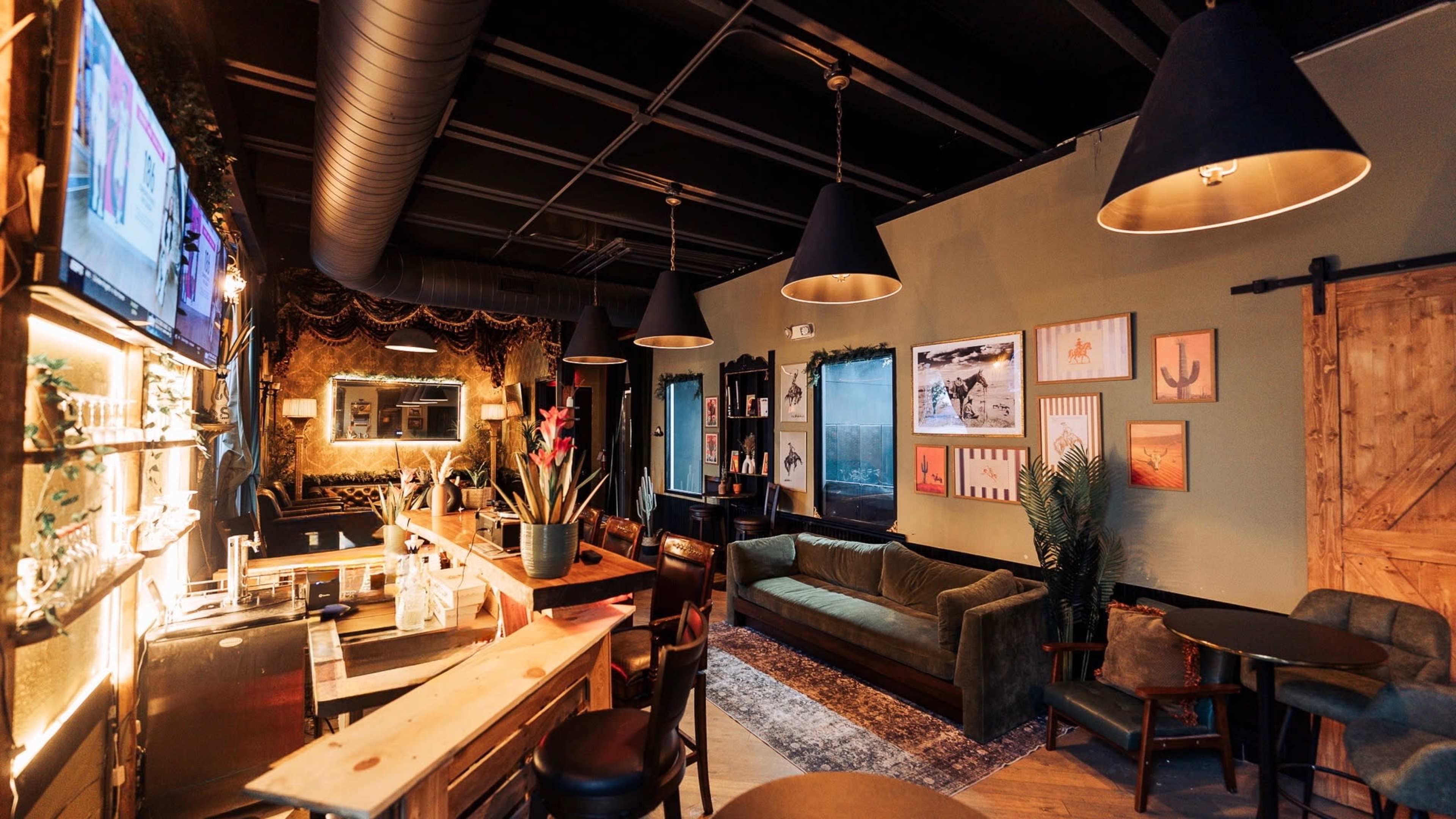 The image shows a stylish bar interior with a cozy seating area, dim lighting, and various framed artworks on the walls.