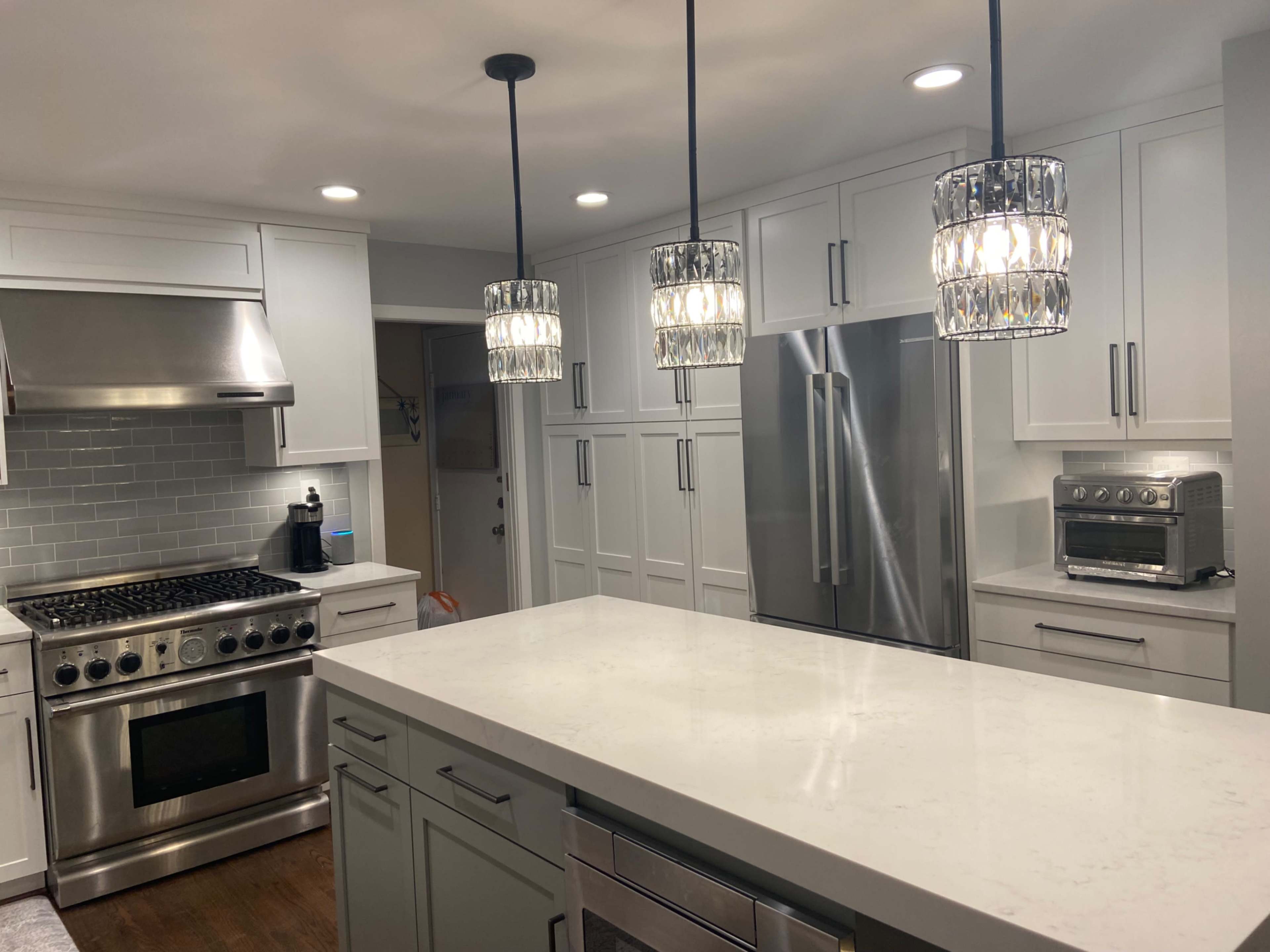 The image depicts a modern kitchen featuring stainless steel appliances, a large island with a white countertop, and three pendant lights hanging above.