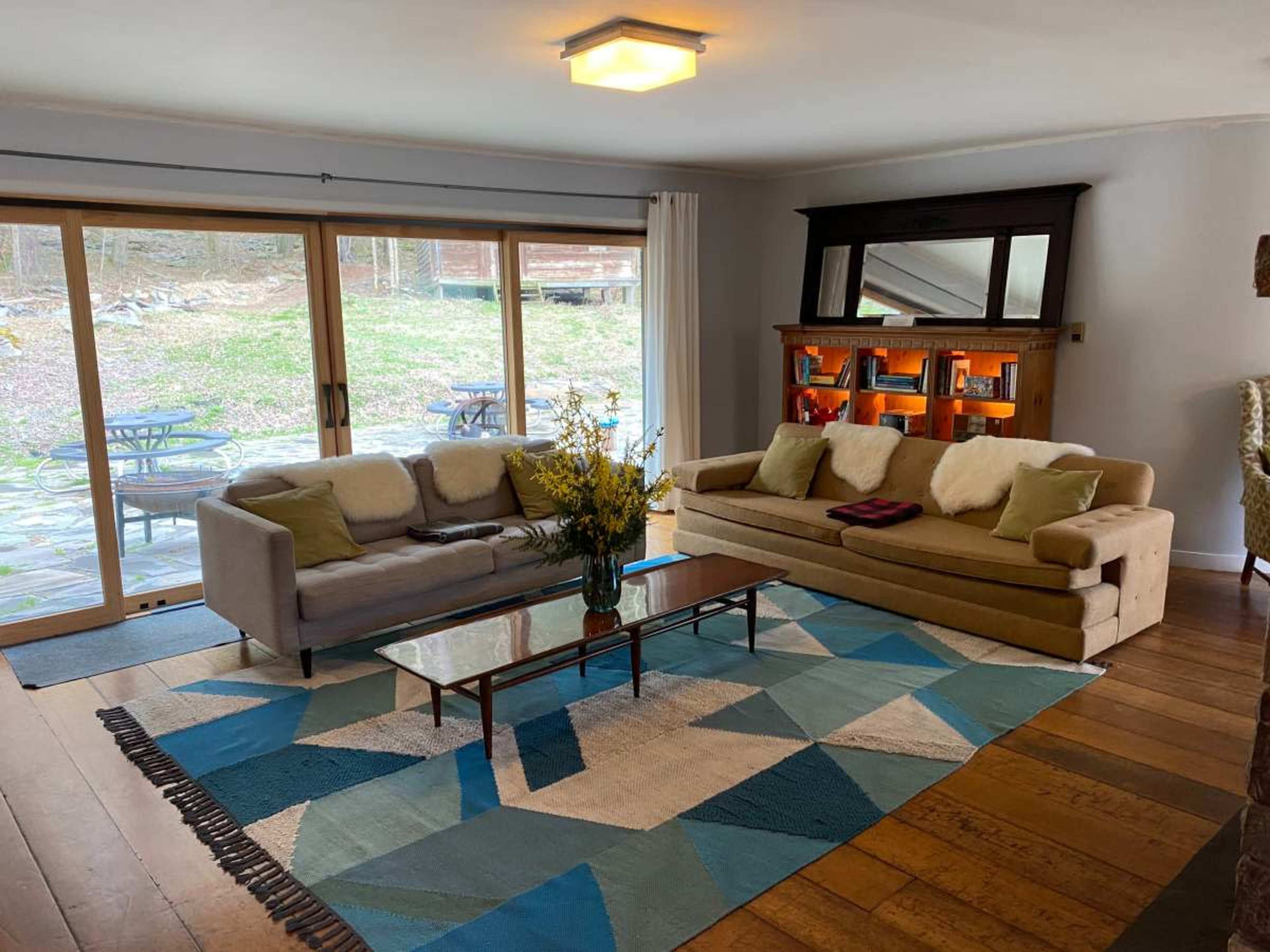 A modern living room features two sofas, a coffee table, a geometric area rug, and large sliding doors that open to an outdoor patio.