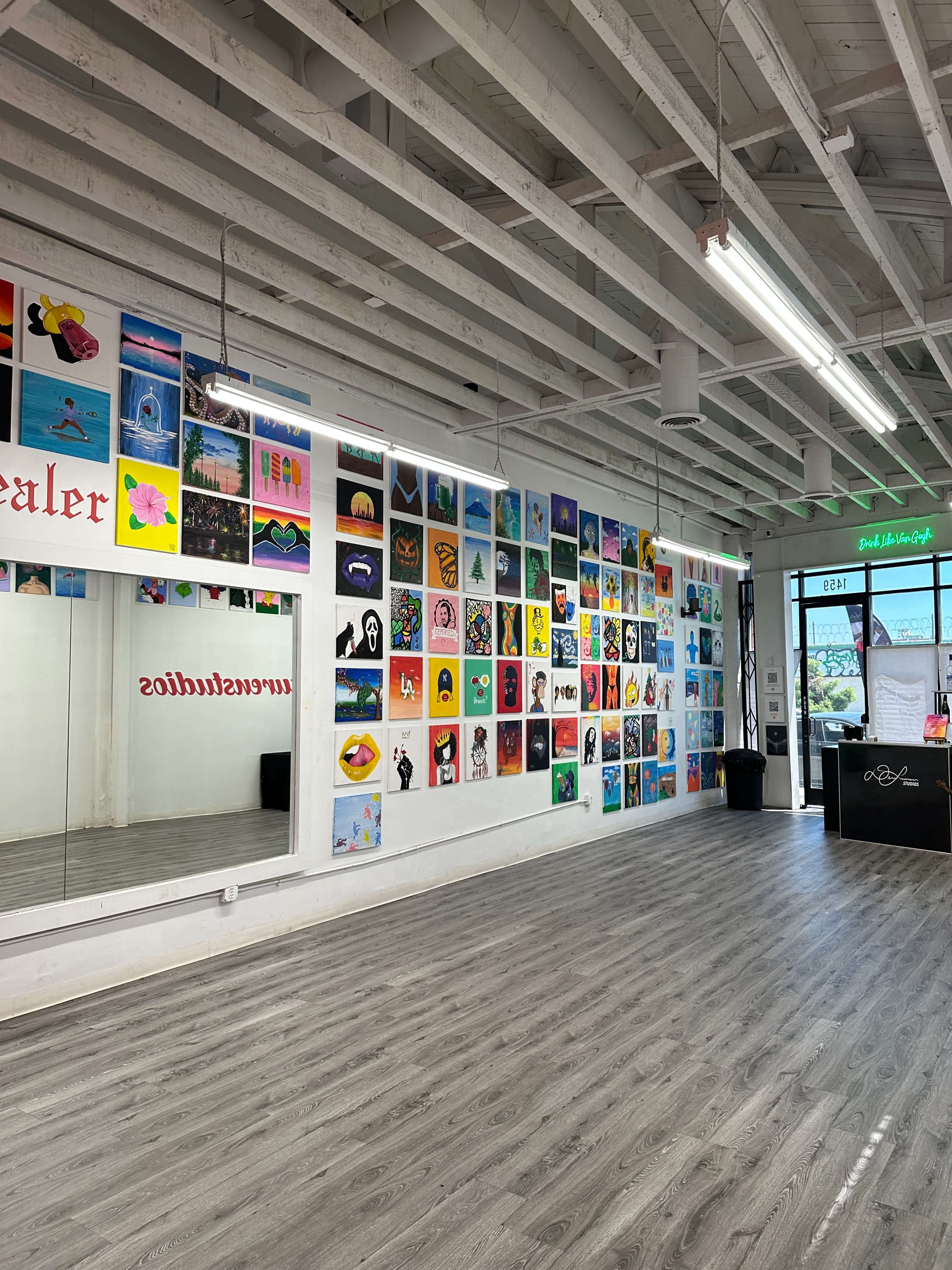 A brightly lit studio with a wall covered in colorful artwork and a large mirror on the opposite side.