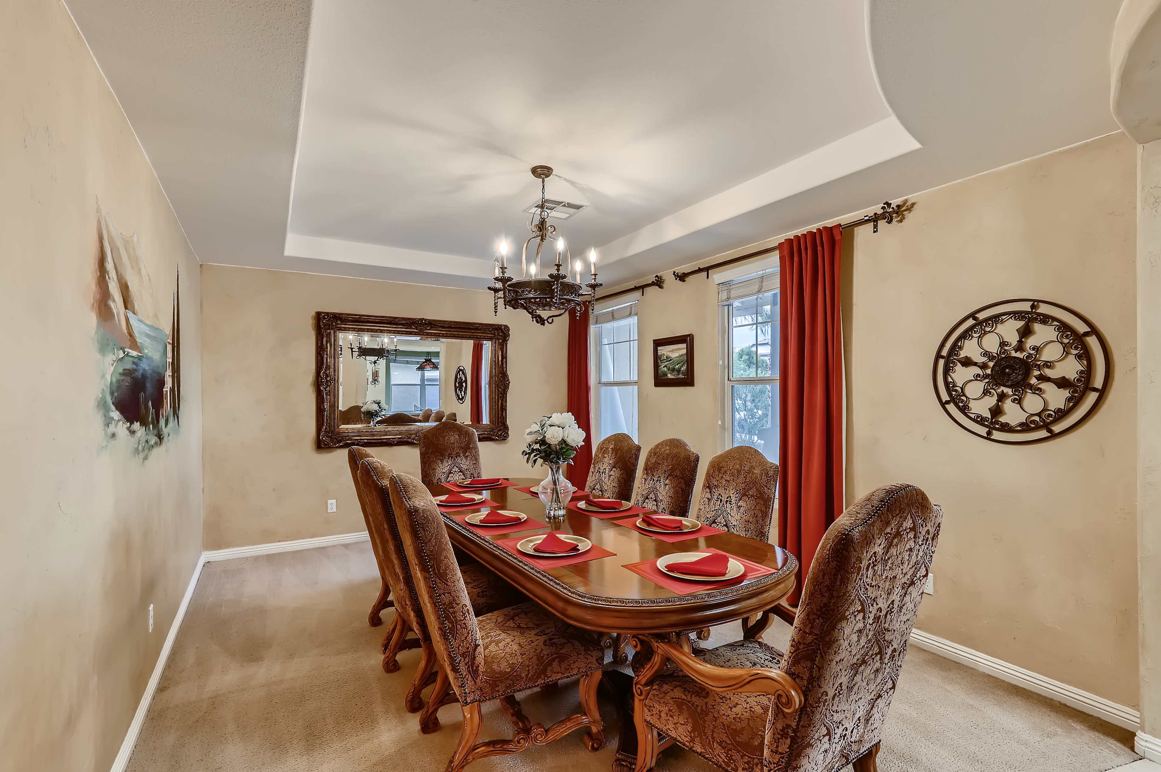 A dining room with a large table set for dinner, surrounded by upholstered chairs, and featuring a chandelier and decorative elements on the walls.