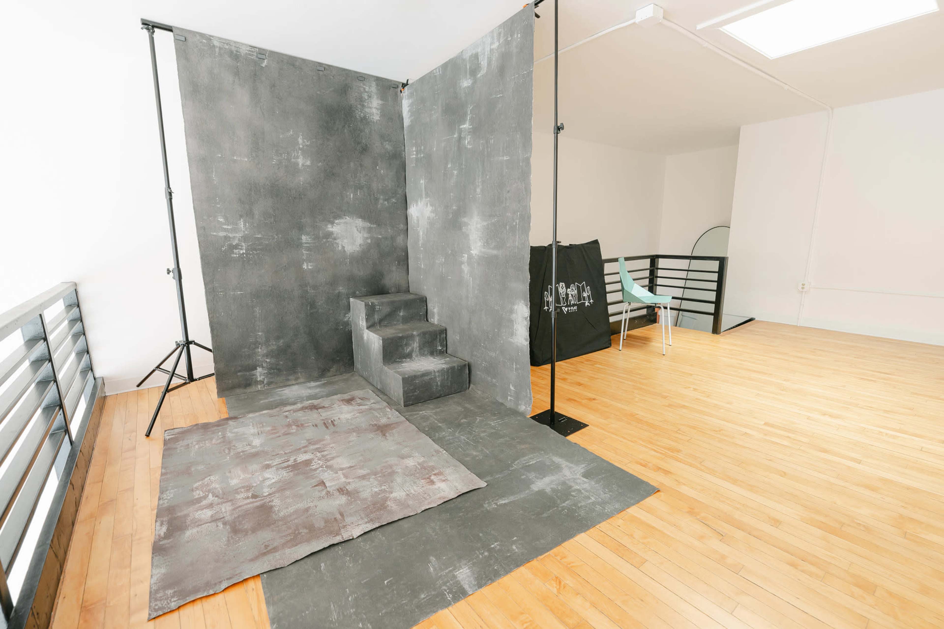 A minimalistic studio space with a gray backdrop, steps, and wooden flooring.