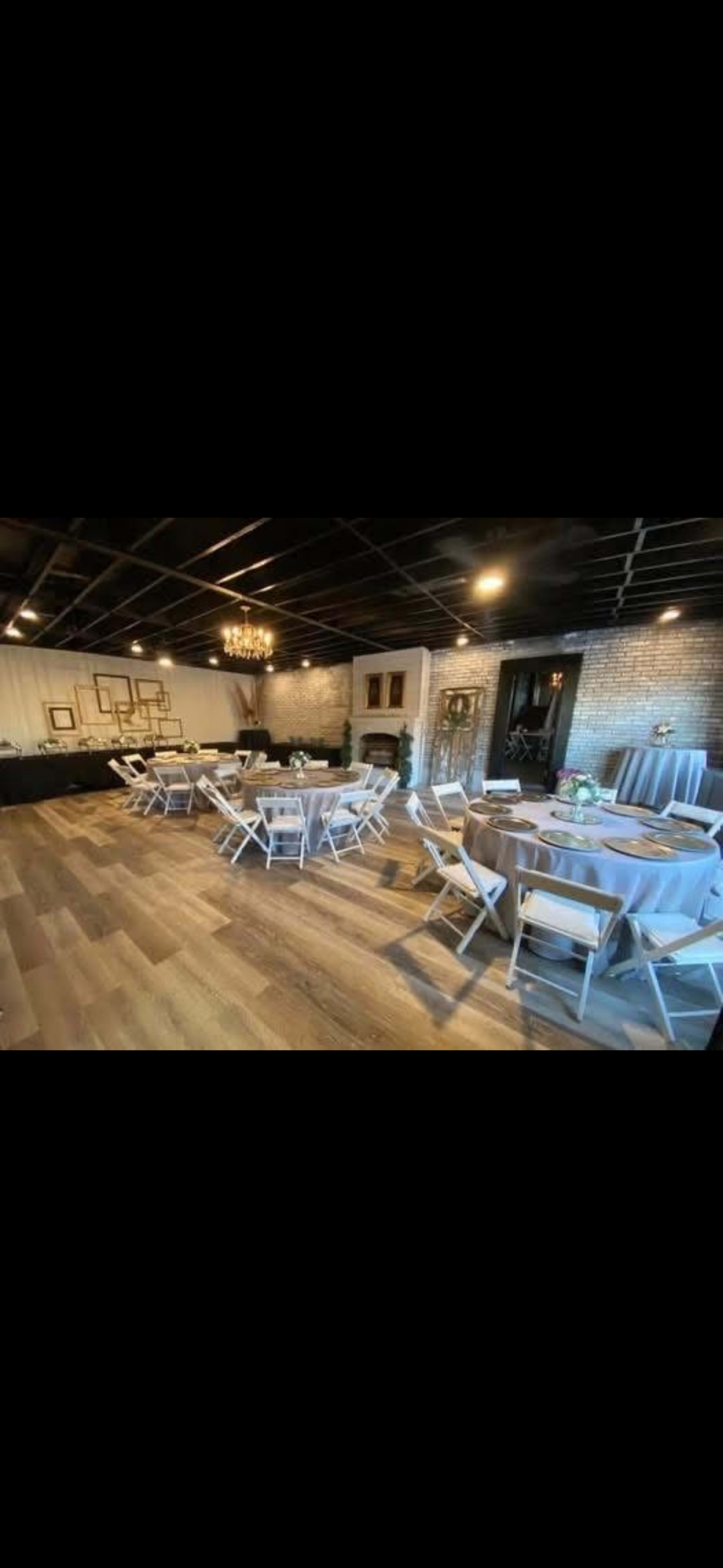 The image shows an elegantly decorated event space with round and rectangular tables set up, white chairs, hardwood flooring, and stylish lighting fixtures.