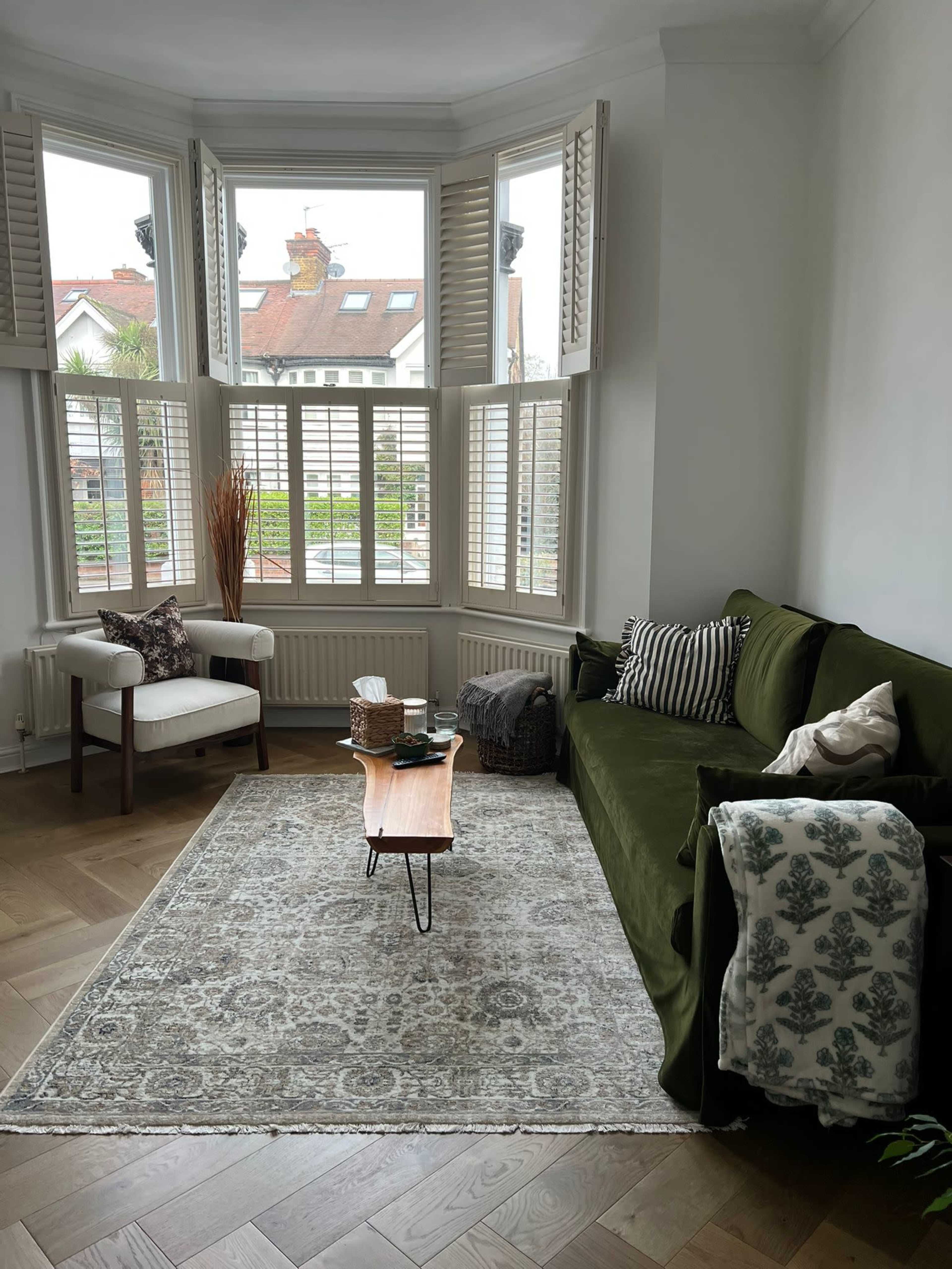 A cozy living room features a green sofa, a wooden coffee table, and large bay windows that overlook a view of the outdoors.